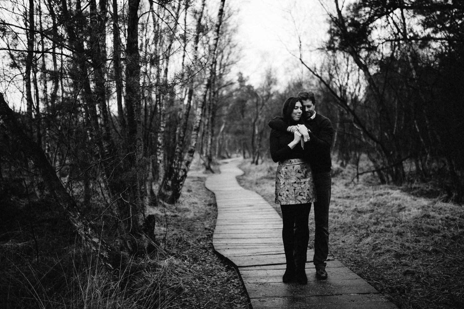 A black and white photo of figures walking on a wooden boardwalk through woods.