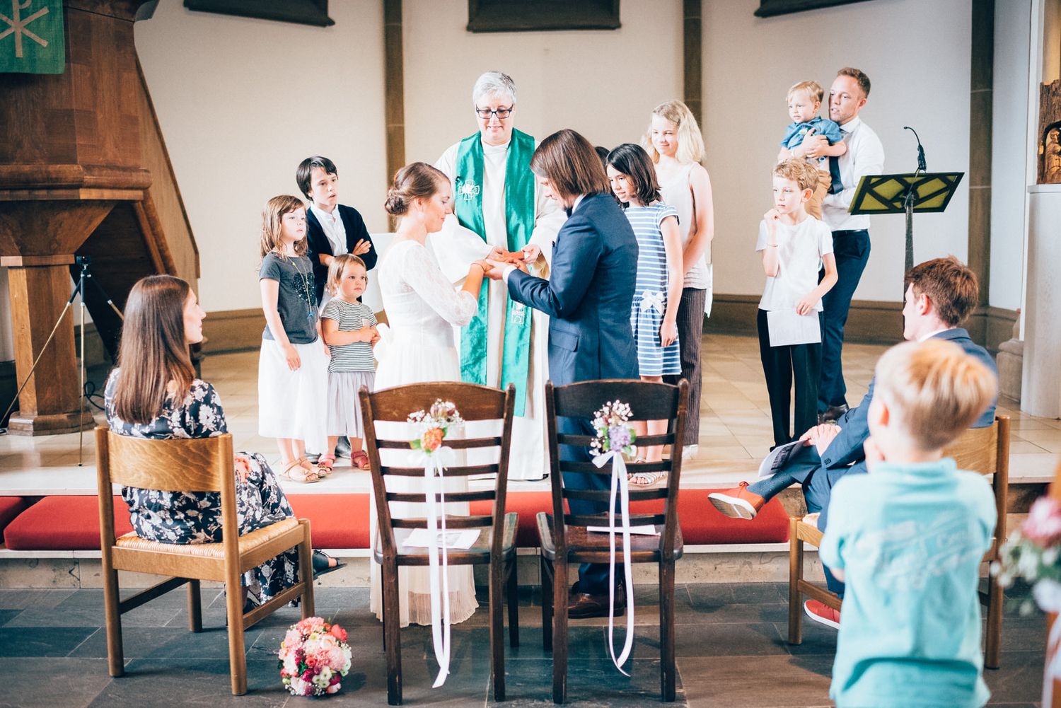 Wedding ceremony in progress at a church with guests and clergy.