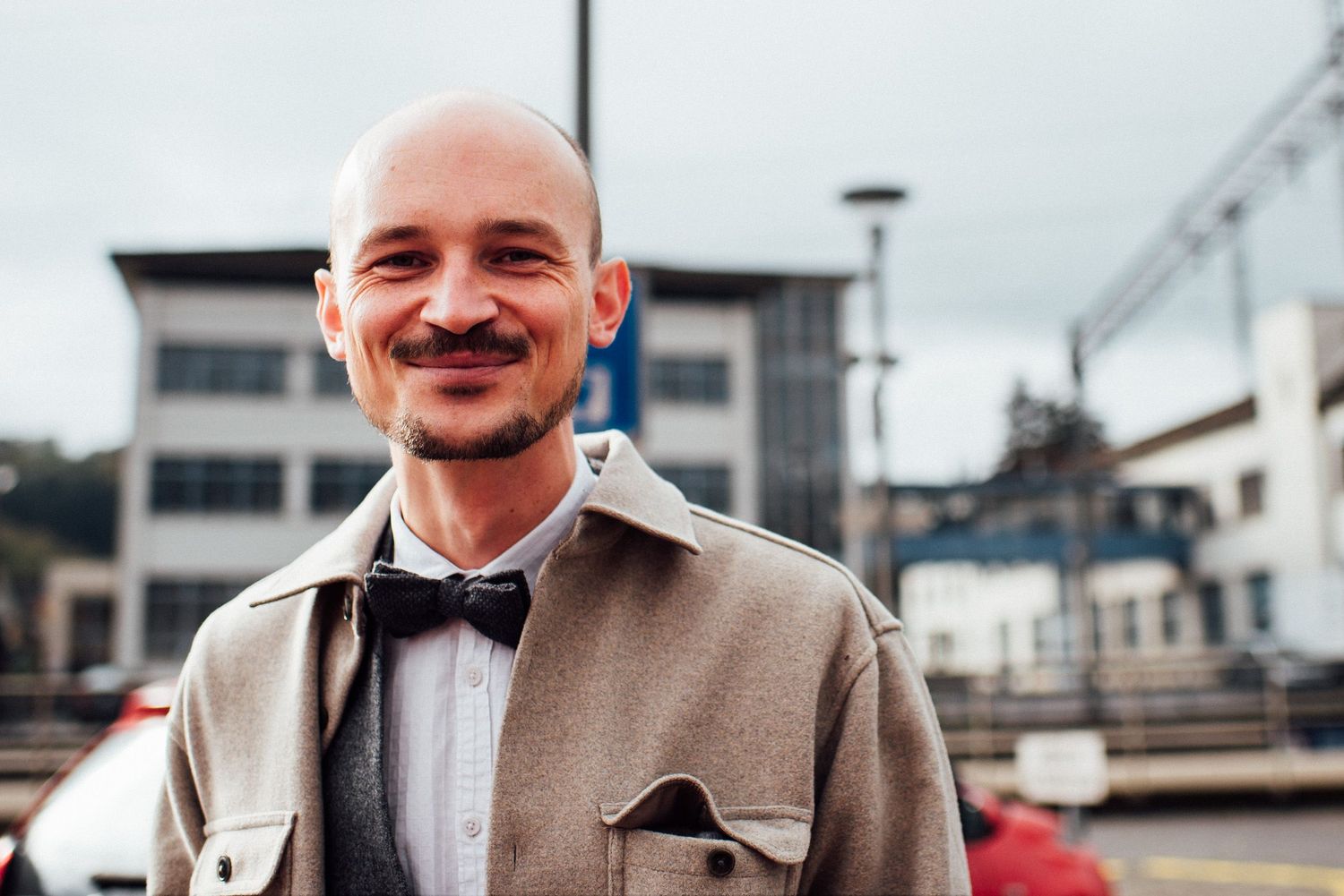Man in formal attire with bowtie smiles on industrial background.