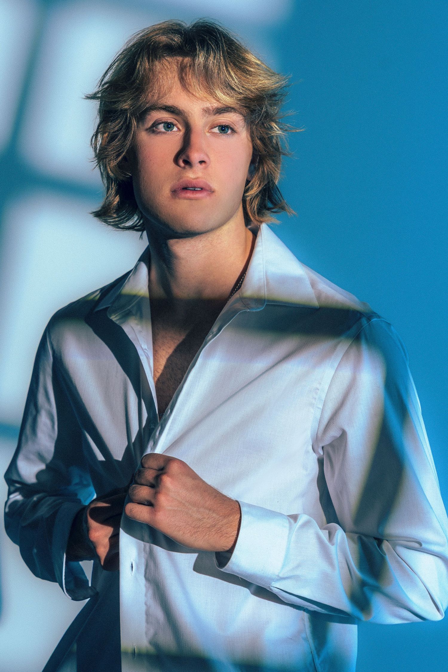Fashion portrait with dramatic blue lighting and white button-down shirt against blue background.