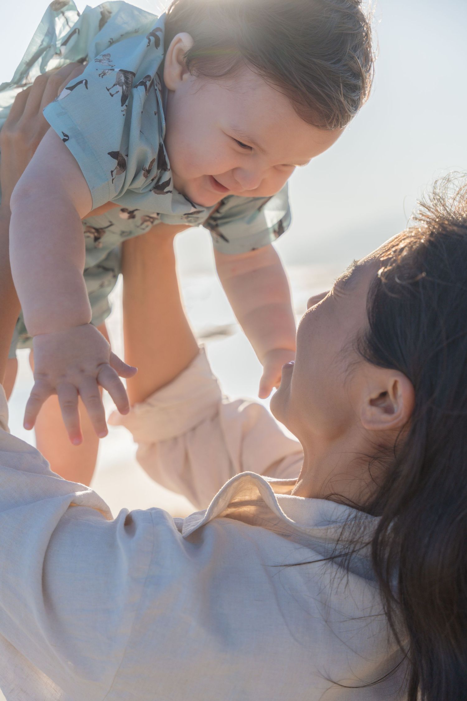 Tender moment between parent and baby against bright sunlit background.