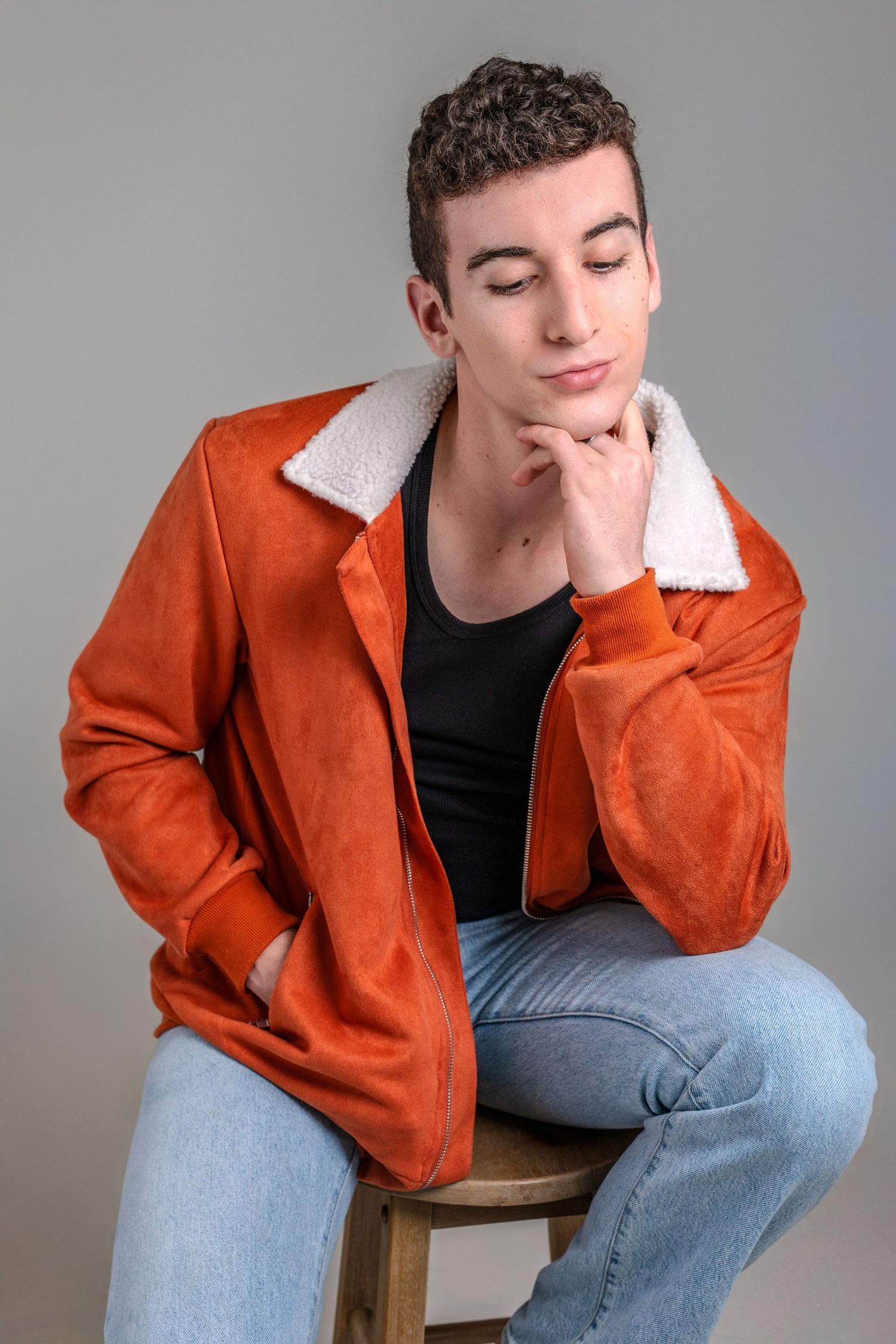 Person in orange jacket and jeans sitting on wooden stool in contemplative poses.