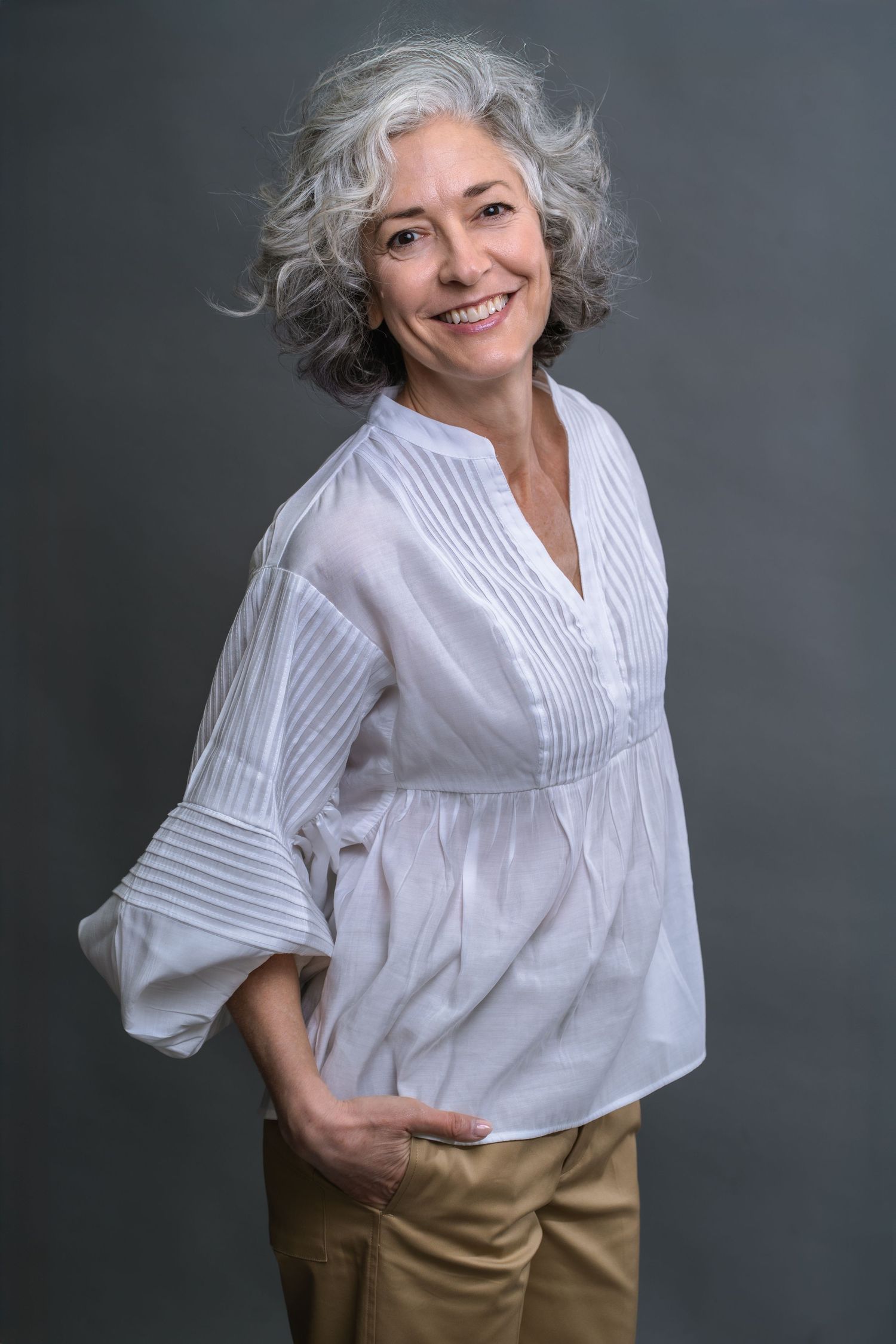 A series of studio portraits showing a person with silver hair wearing a white blouse and tan pants against a gray backdrop.