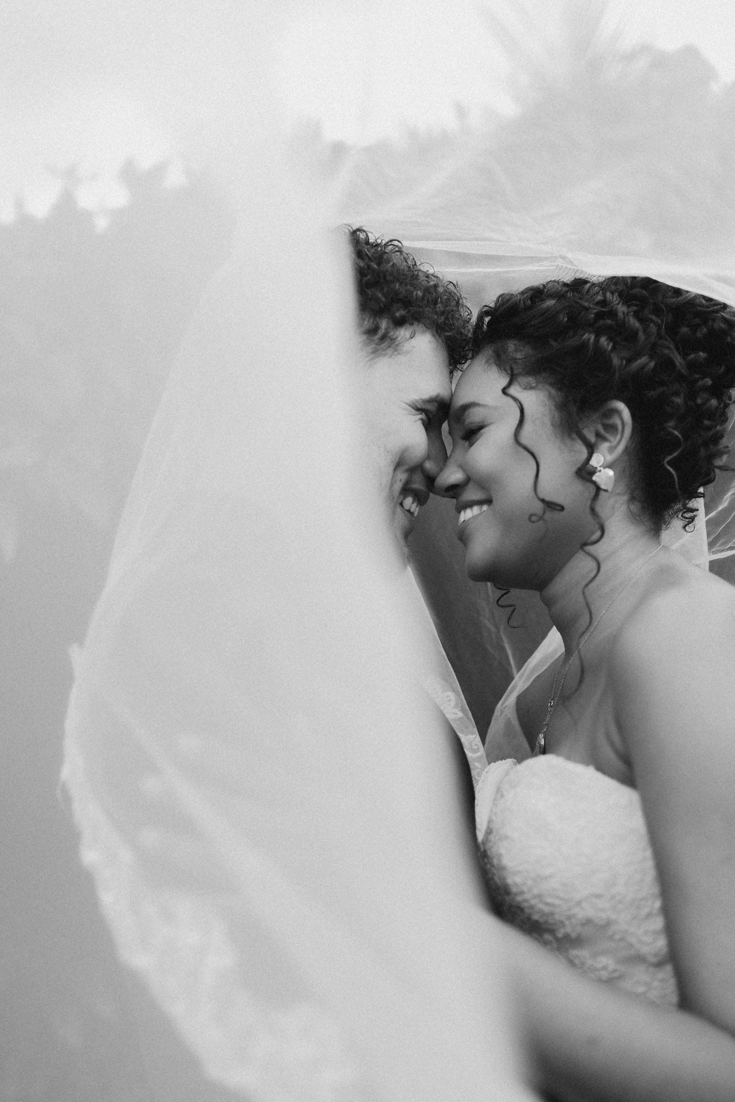 Artistic black and white wedding photo capturing intimate moment through sheer veil.