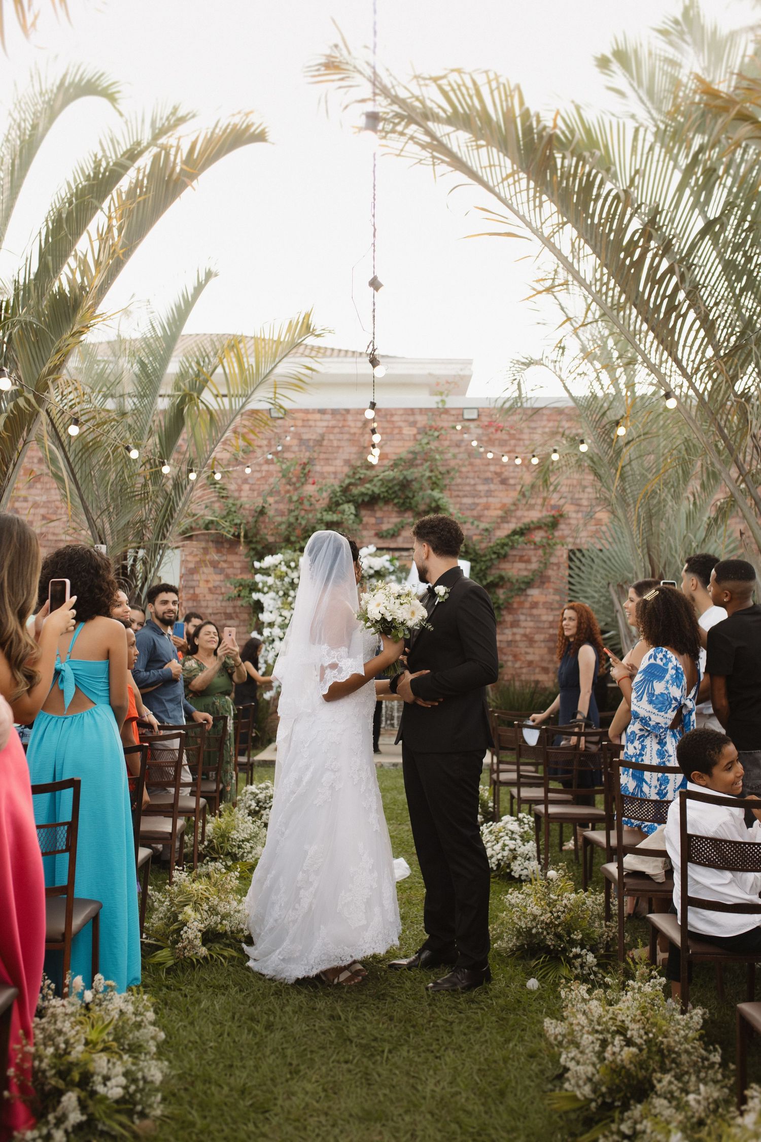 Guests celebrating at an outdoor wedding with tropical decor and string lights.