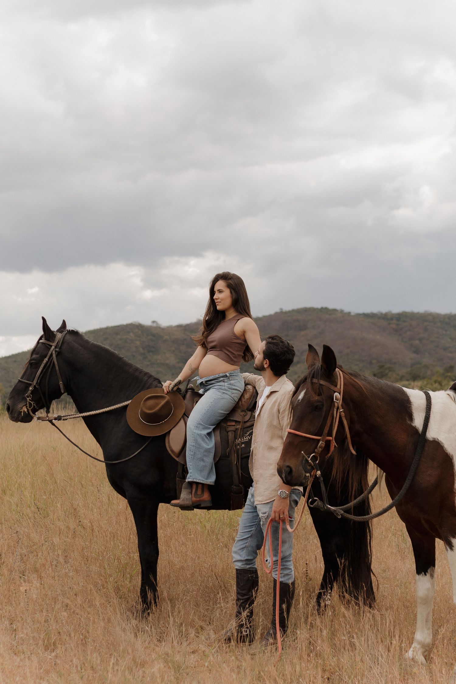 Riders prepare to mount horses in a golden field with mountains in background.