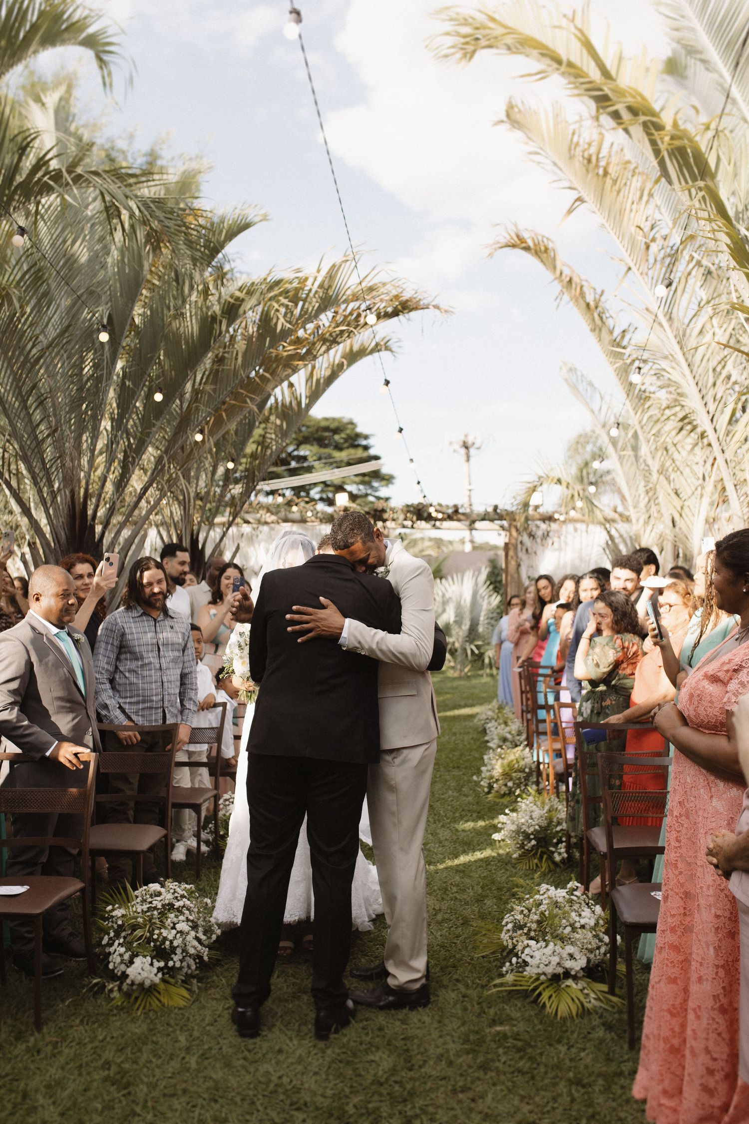 Wedding guests gather outdoors under palm trees for an intimate ceremony celebration.