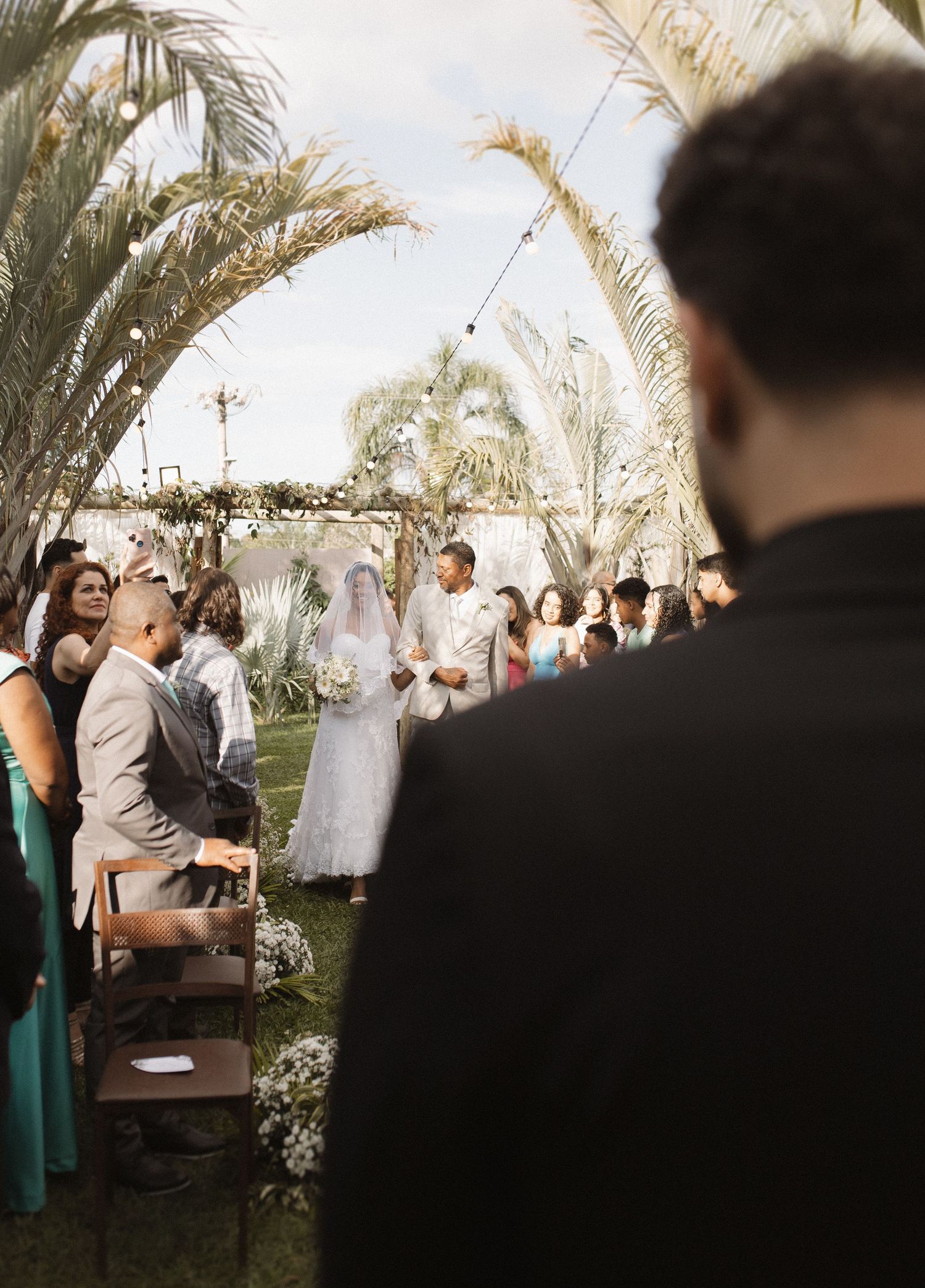 Wedding guests seated outdoors under palm trees during ceremony.