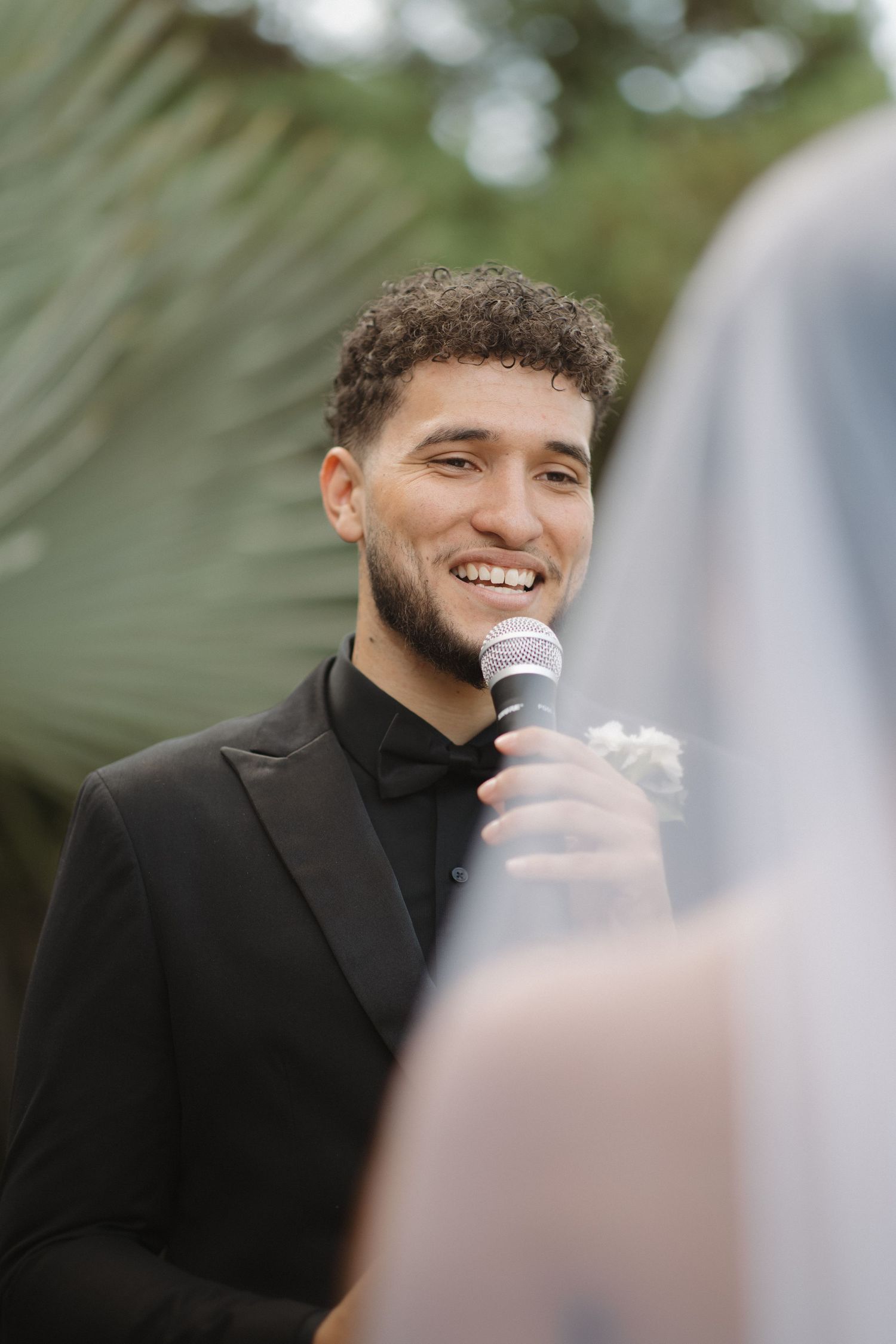 Close-up shots of a groom in a black suit speaking during an outdoor wedding ceremony.