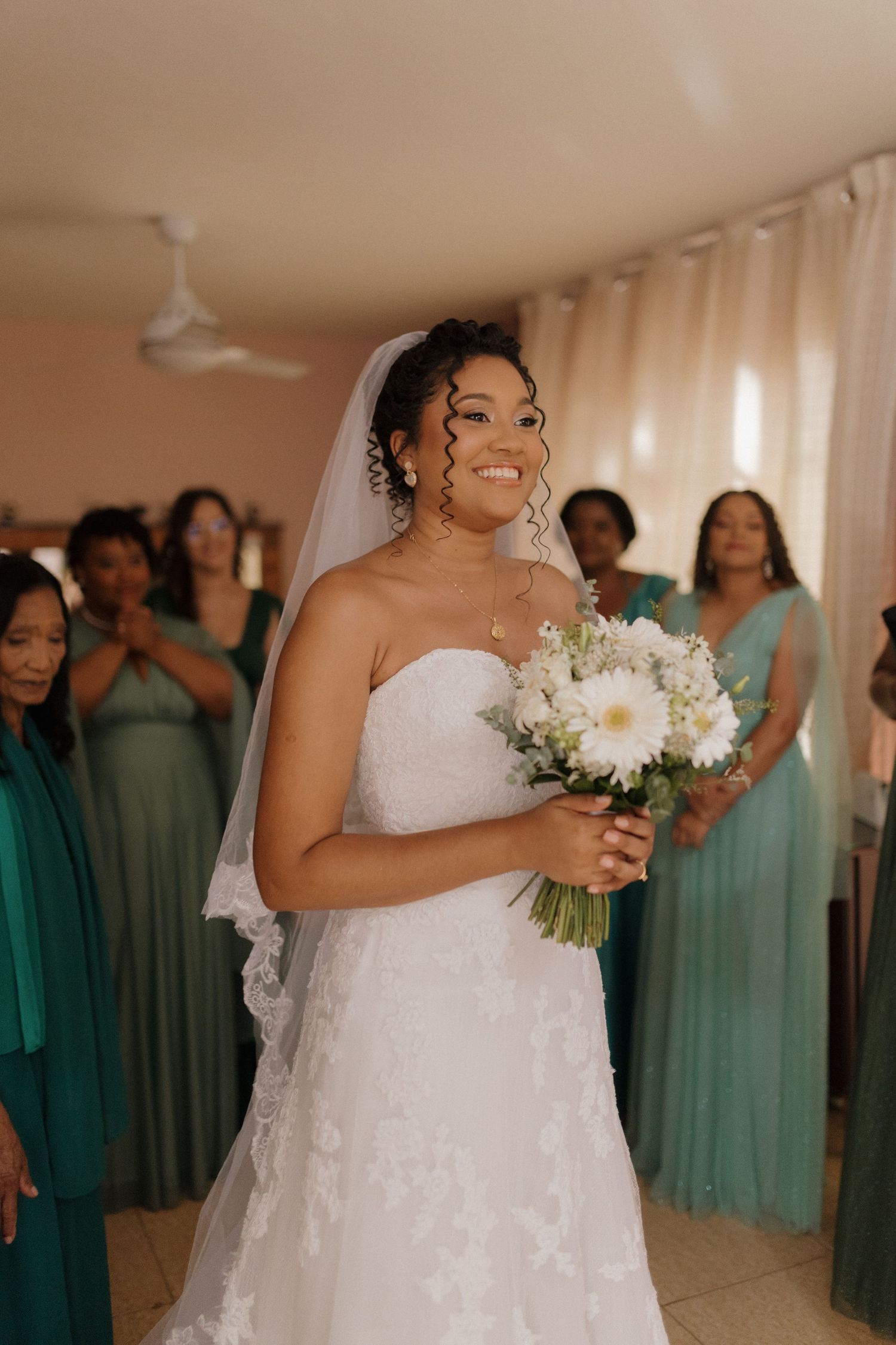 Wedding party members in teal bridesmaid dresses gather around a bride holding a white bouquet.
