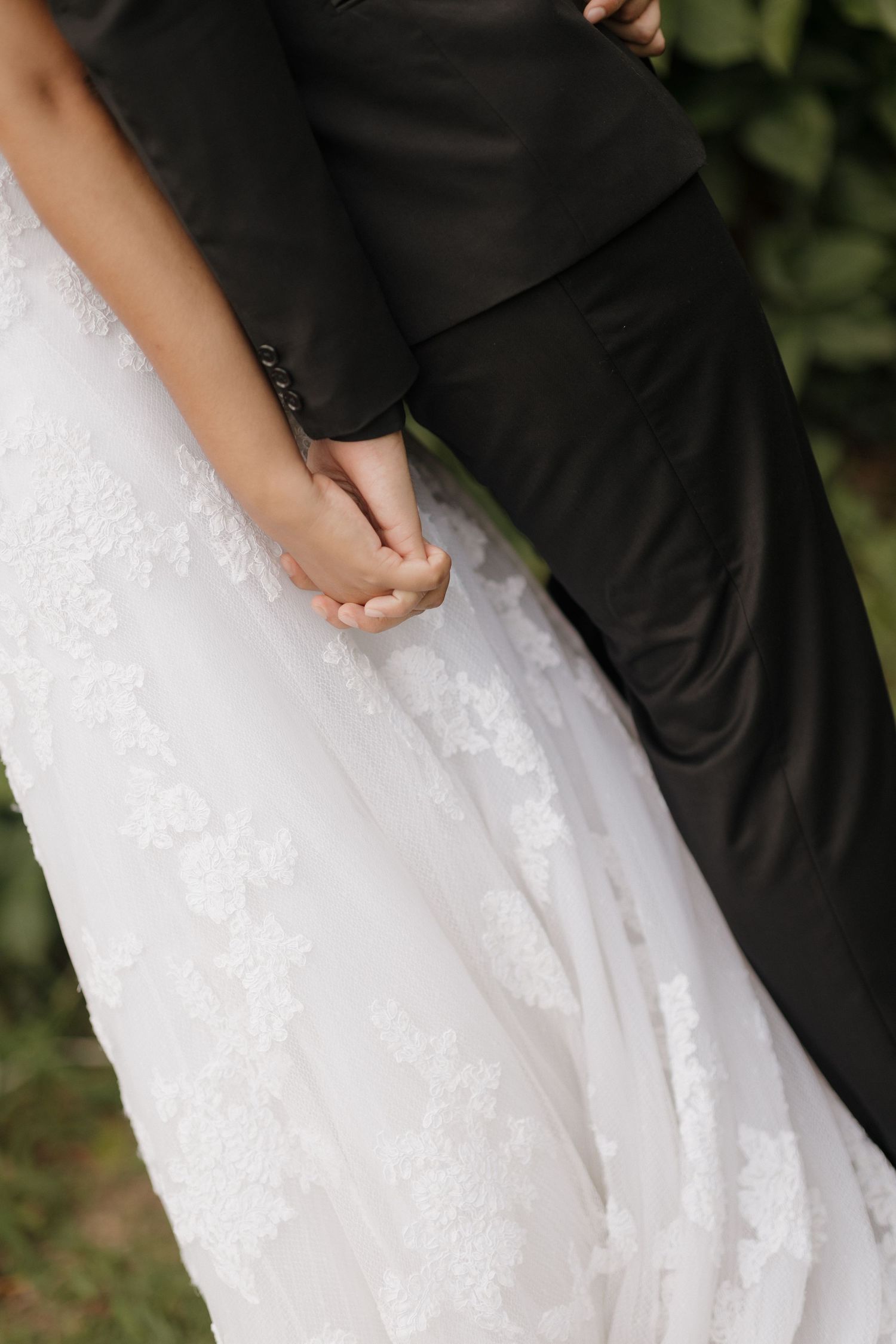 Close-up detail of a bride in a white lace wedding dress standing next to someone in a black suit.