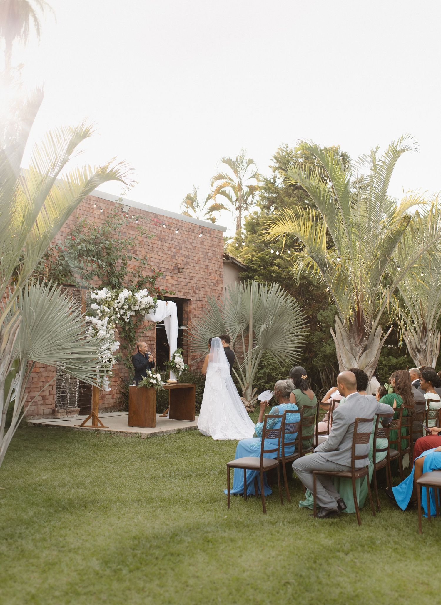 Outdoor wedding venue with palm trees and blue chairs set up on grass lawn.