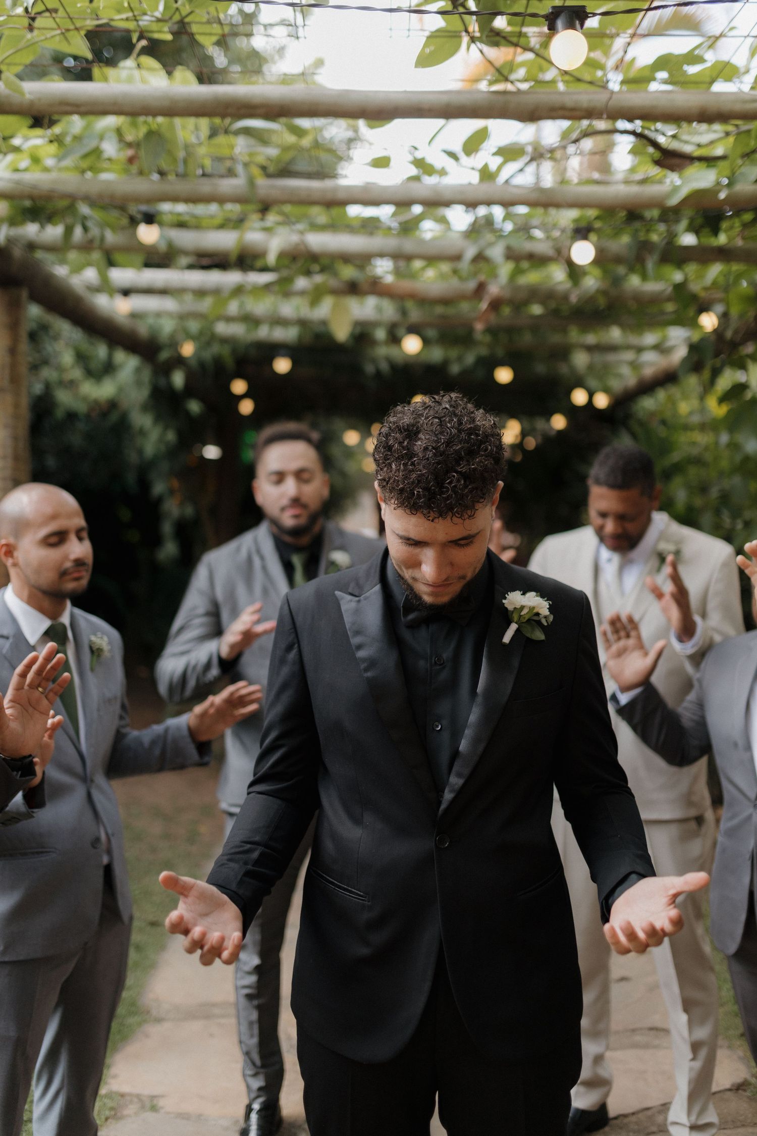 Groomsmen in dark suits dance and celebrate at an outdoor wedding venue.