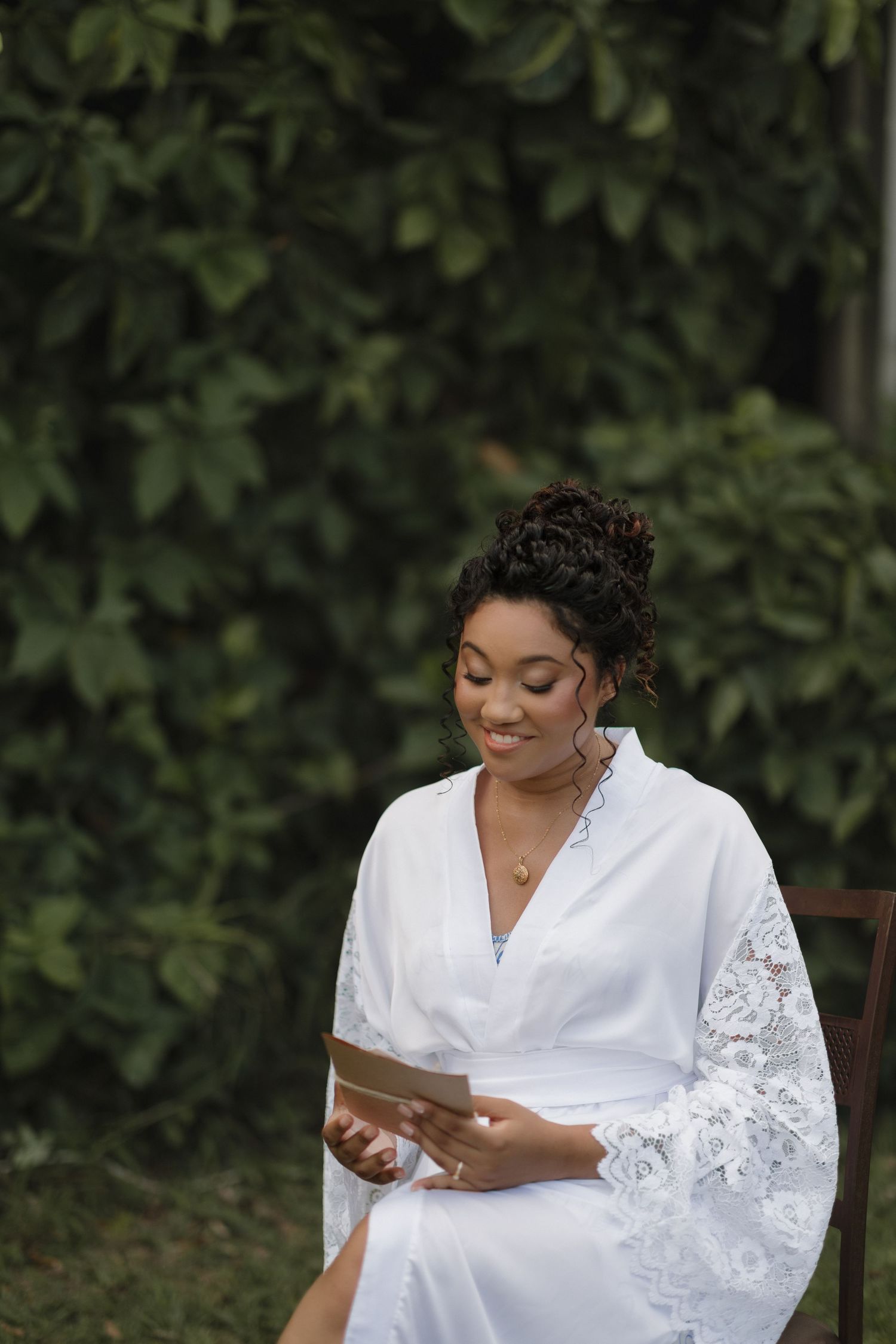 A person in a white lace robe sits in a garden setting while looking at their phone.