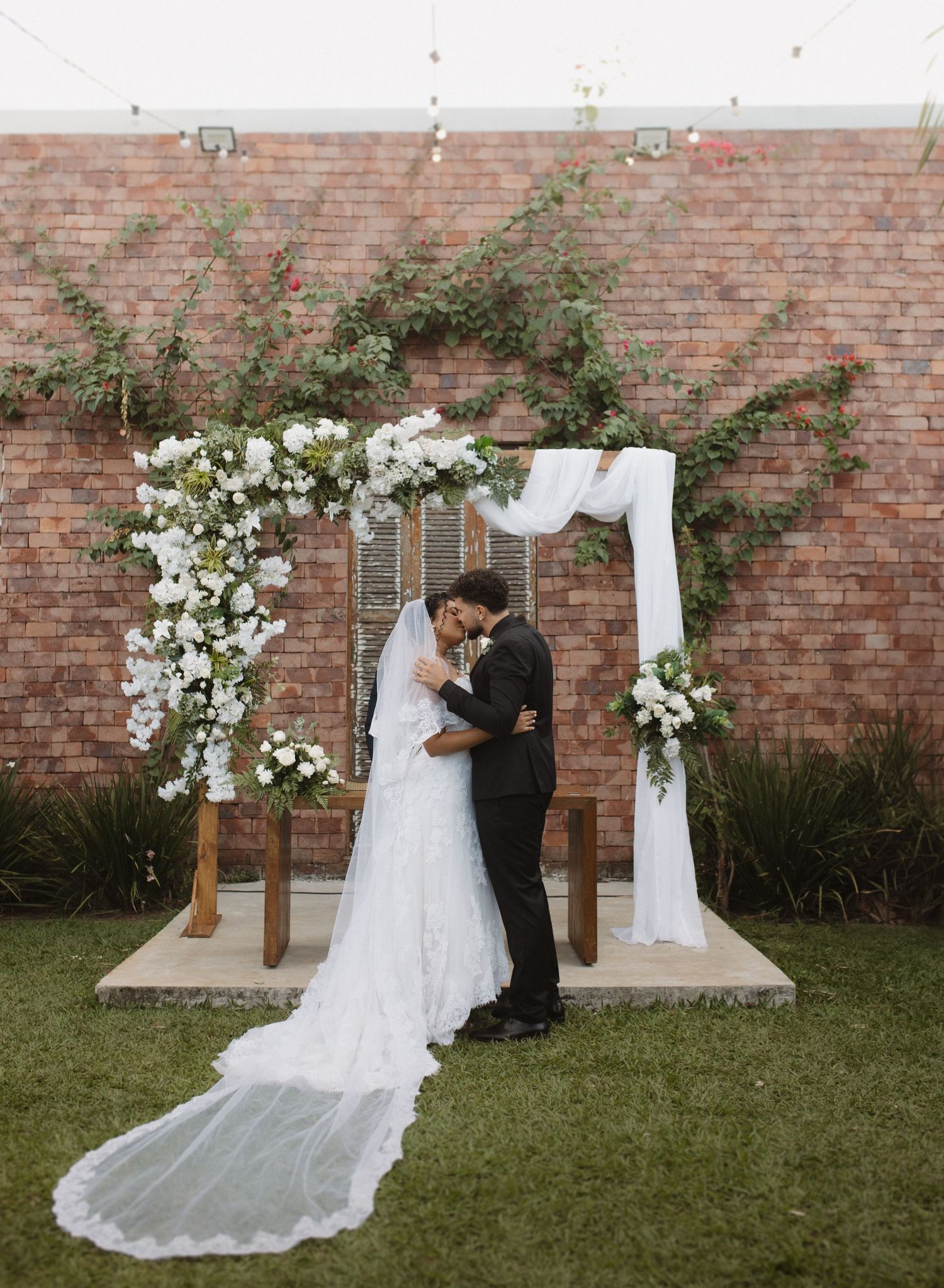 Intimate wedding ceremony in front of a brick wall with white floral arch and drapery.