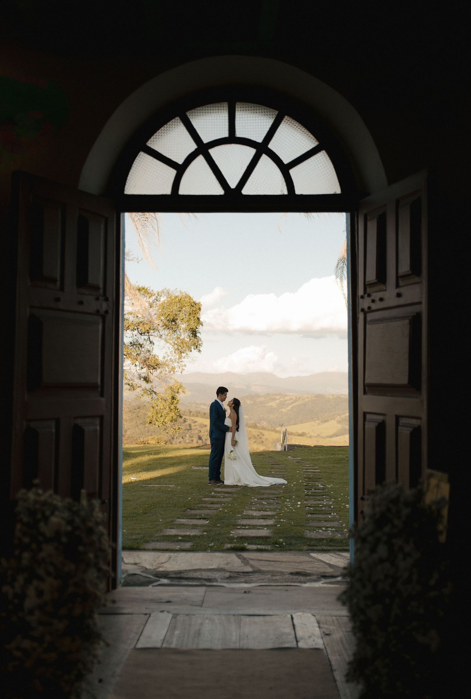Bride and groom silhouetted in arched doorway with rolling hills and dramatic sky backdrop at outdoor wedding venue.