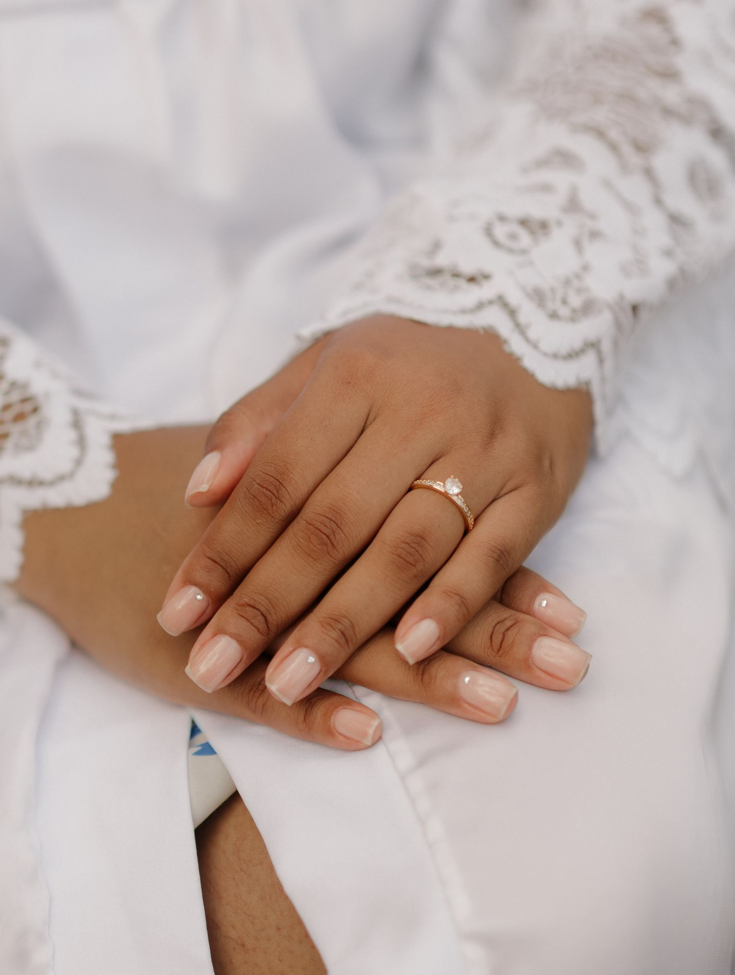 Close-up of hands with a wedding ring resting on white lace fabric.
