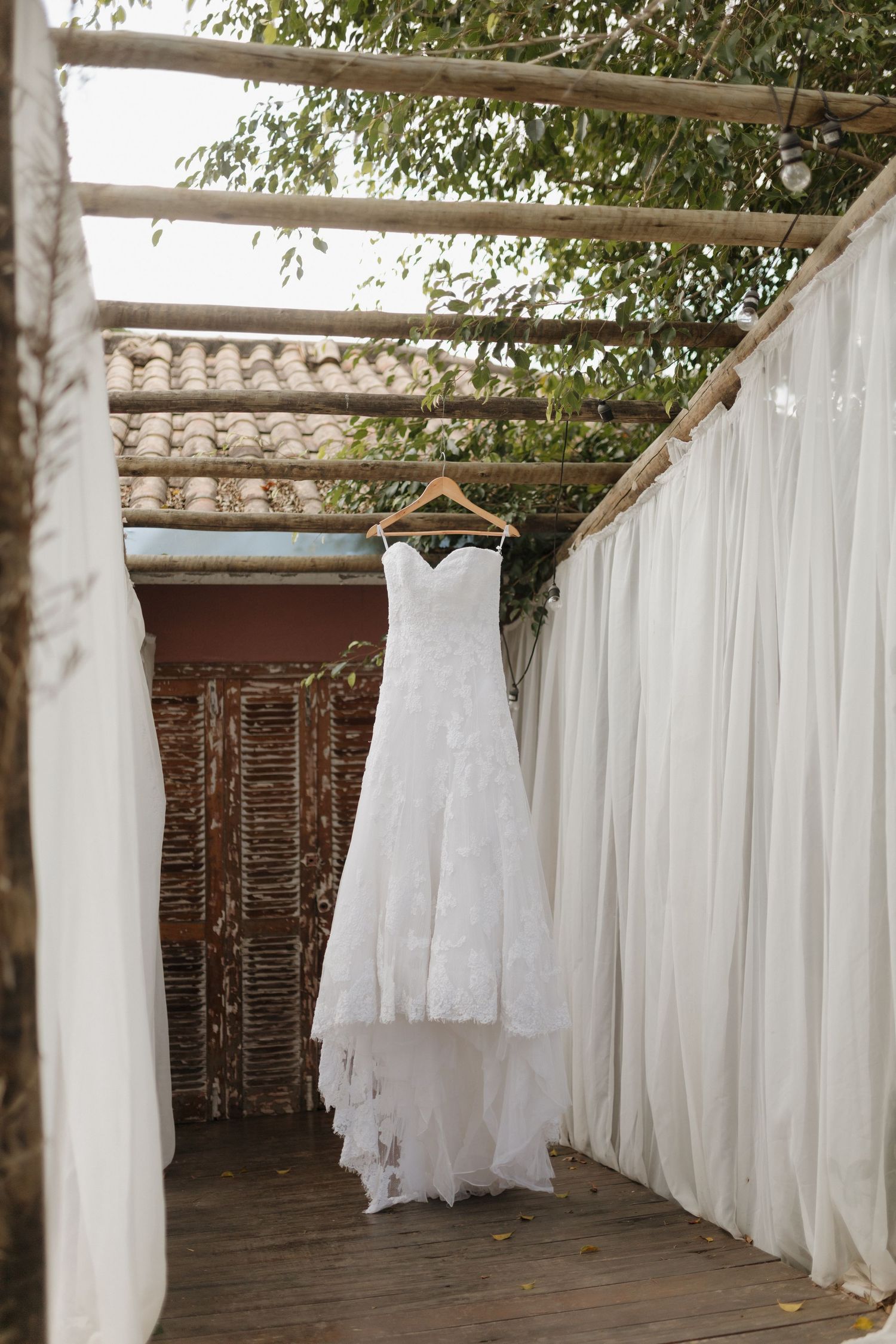 White wedding dresses hanging in a rustic outdoor dressing area with flowing curtains.
