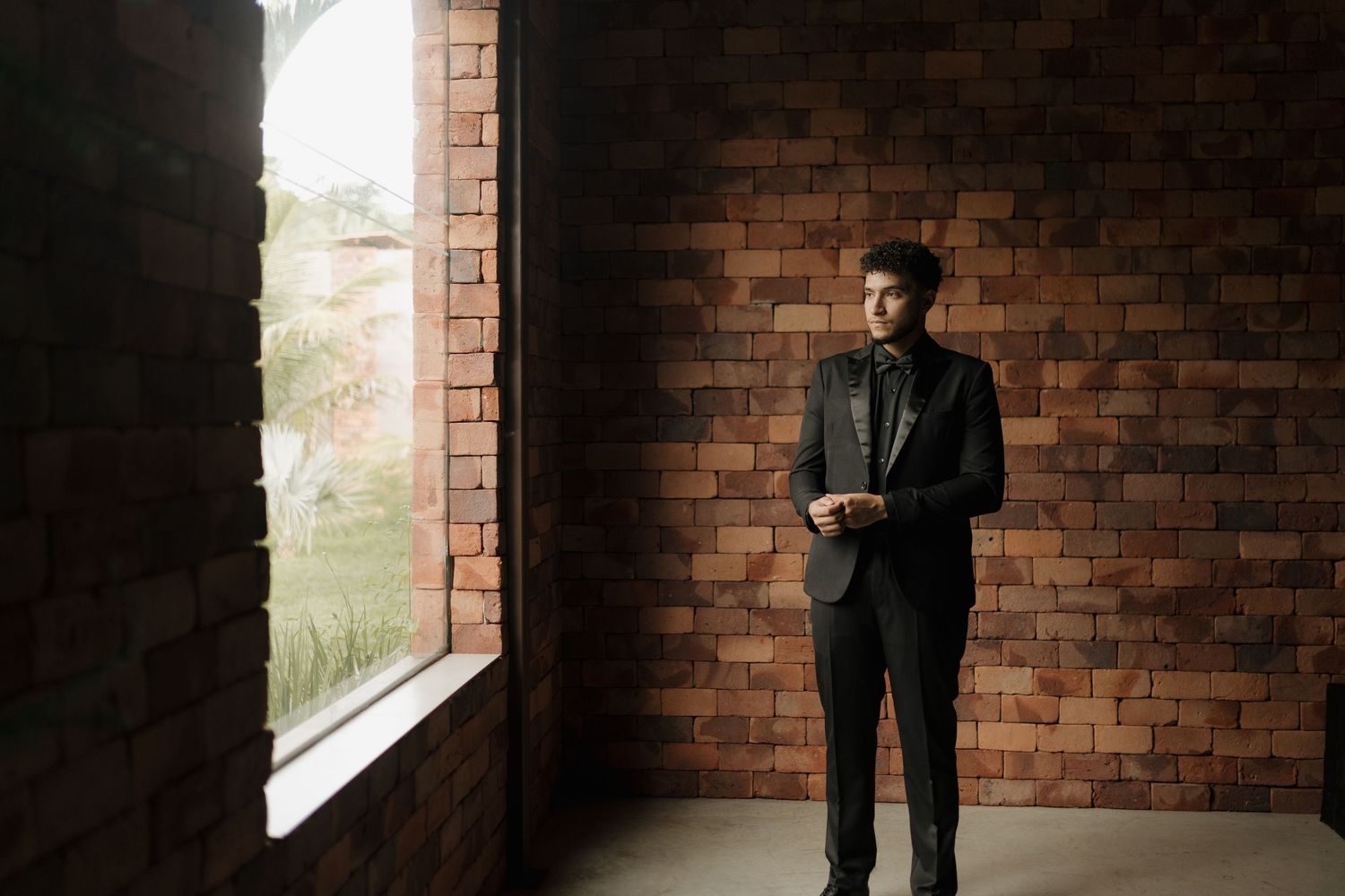 A silhouetted figure stands contemplatively in a brick-walled room with natural window light.
