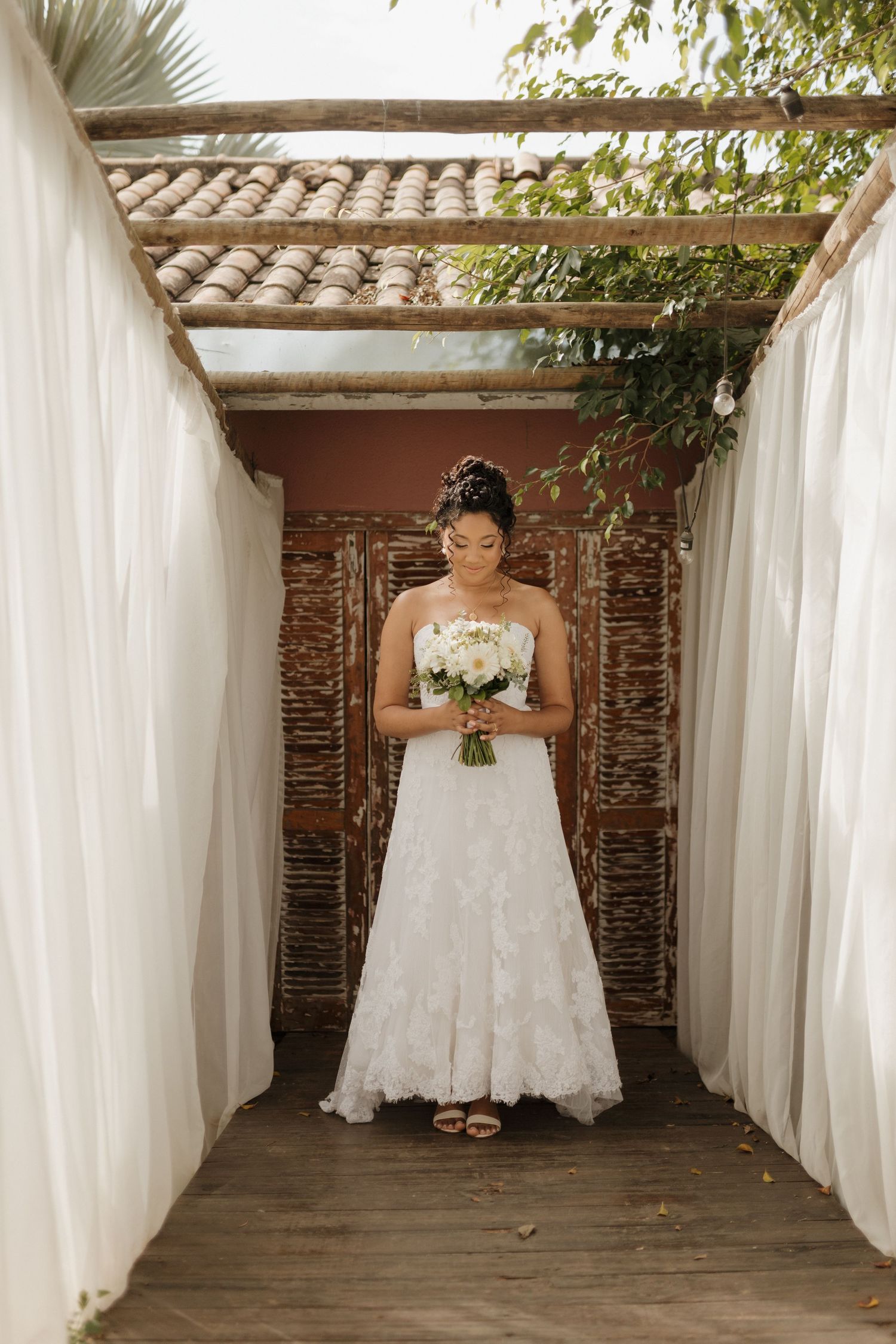 Bride holding a white bouquet poses in sequence against rustic backdrop with flowing curtains.