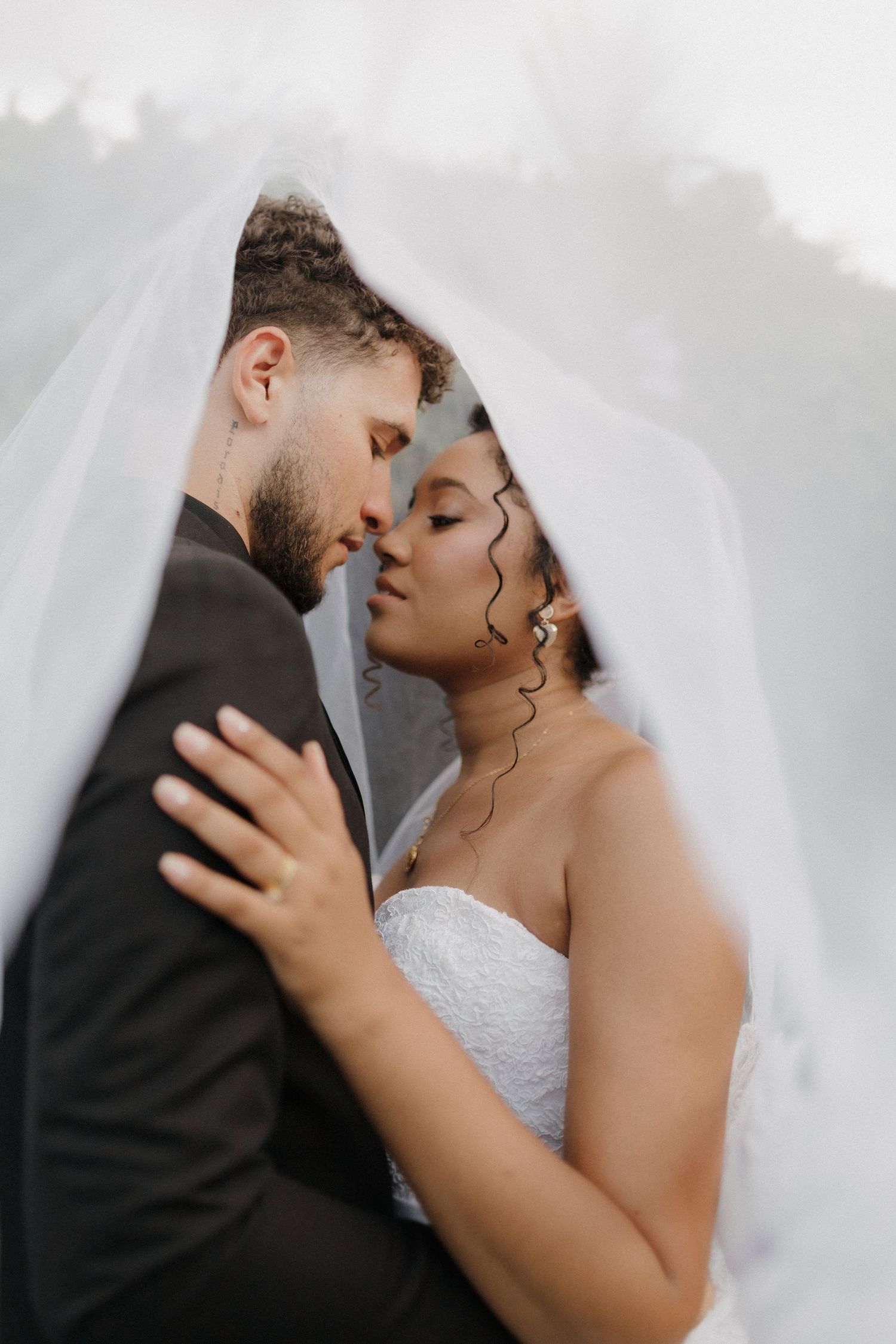 Dreamy wedding portrait with couple under flowing white veil against soft background.