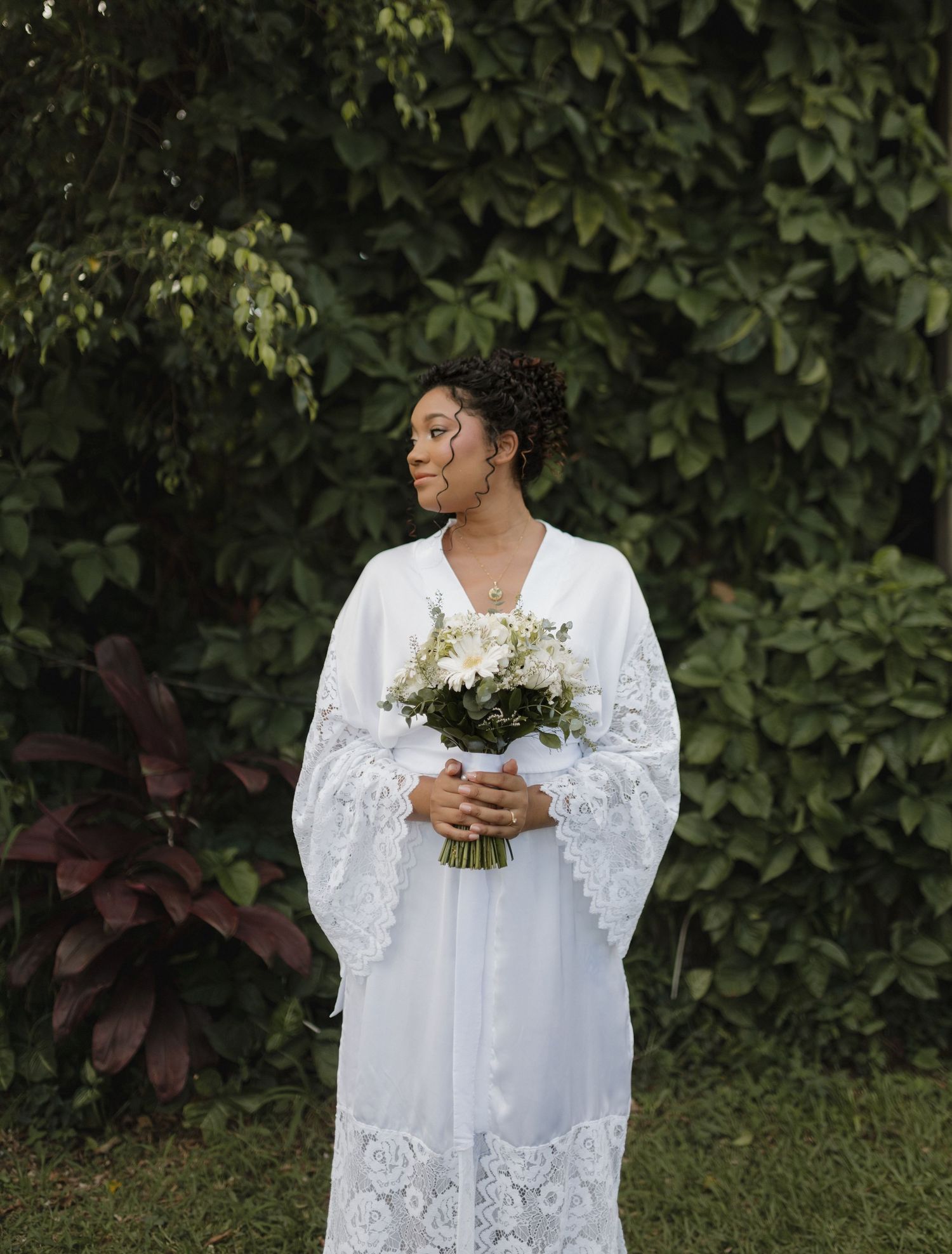 Someone in a white lace dress holds a delicate bouquet of flowers in a garden setting.