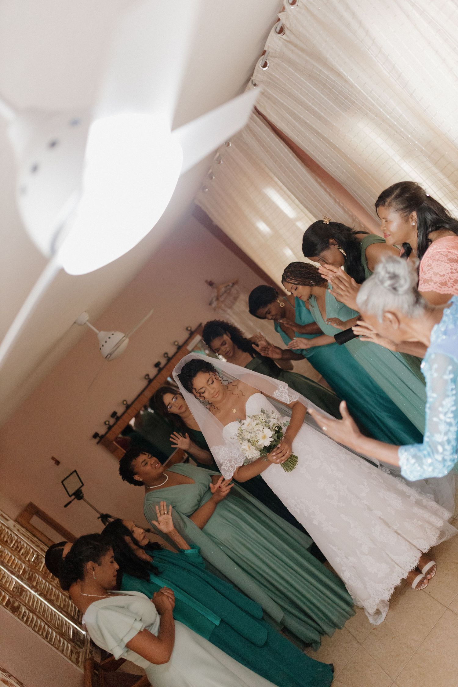 Wedding party poses indoors with bridesmaids wearing teal dresses and bride in white gown.