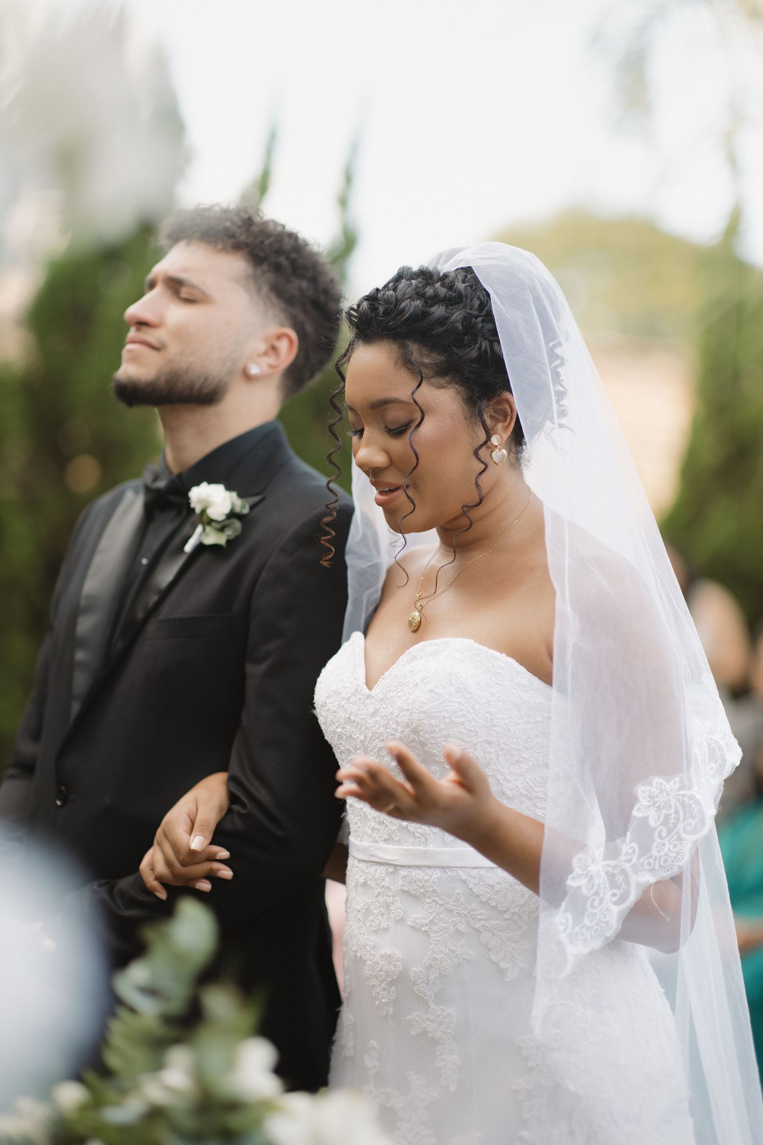 A tender wedding ceremony moment captured outdoors with a couple in formal attire exchanging vows.