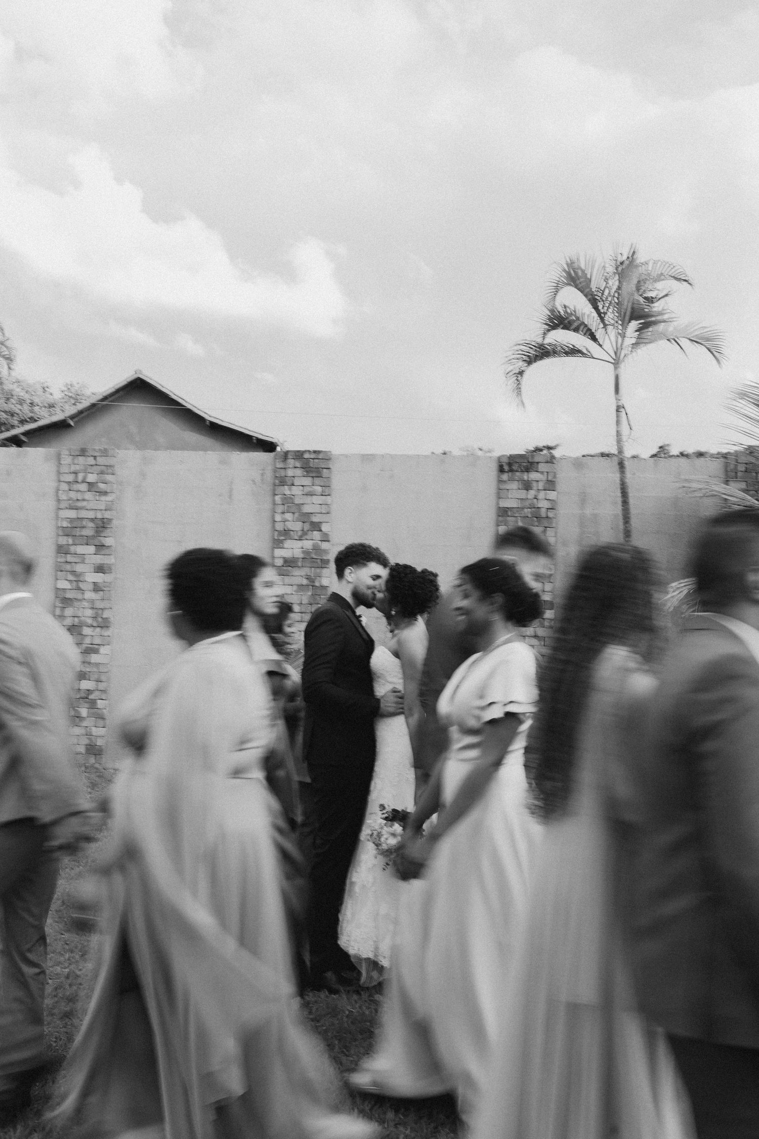 Motion blur captures wedding party walking in formal attire against cloudy sky.
