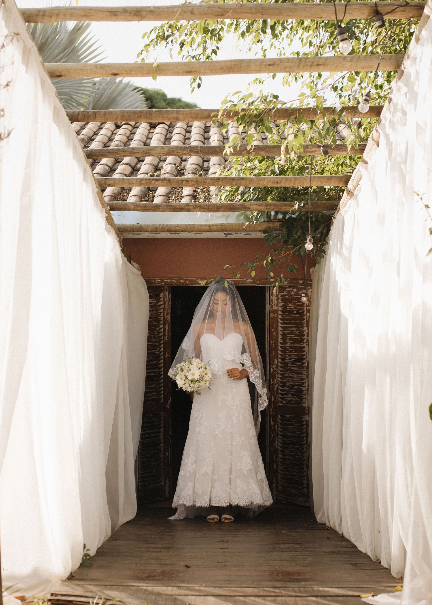 White wedding dresses displayed on hangers in a rustic venue with brick walls and draped fabric.