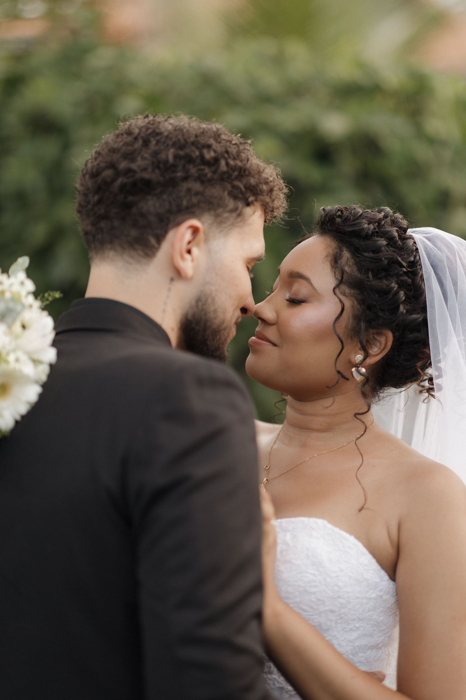 Intimate wedding portrait showing couple in tender close-up moment against natural backdrop.