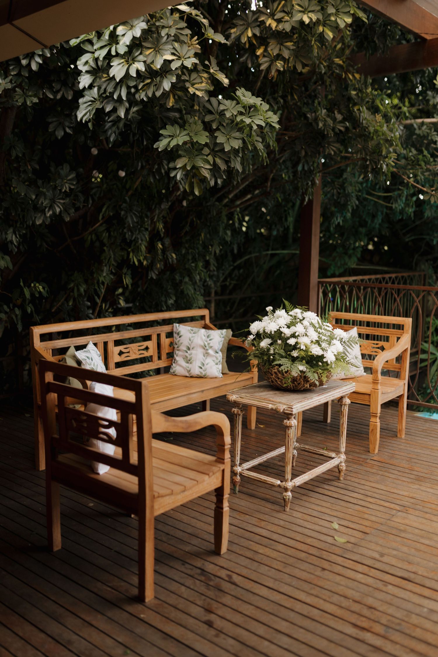 Wooden benches and tables arranged on a deck with floral decorations for an outdoor event.