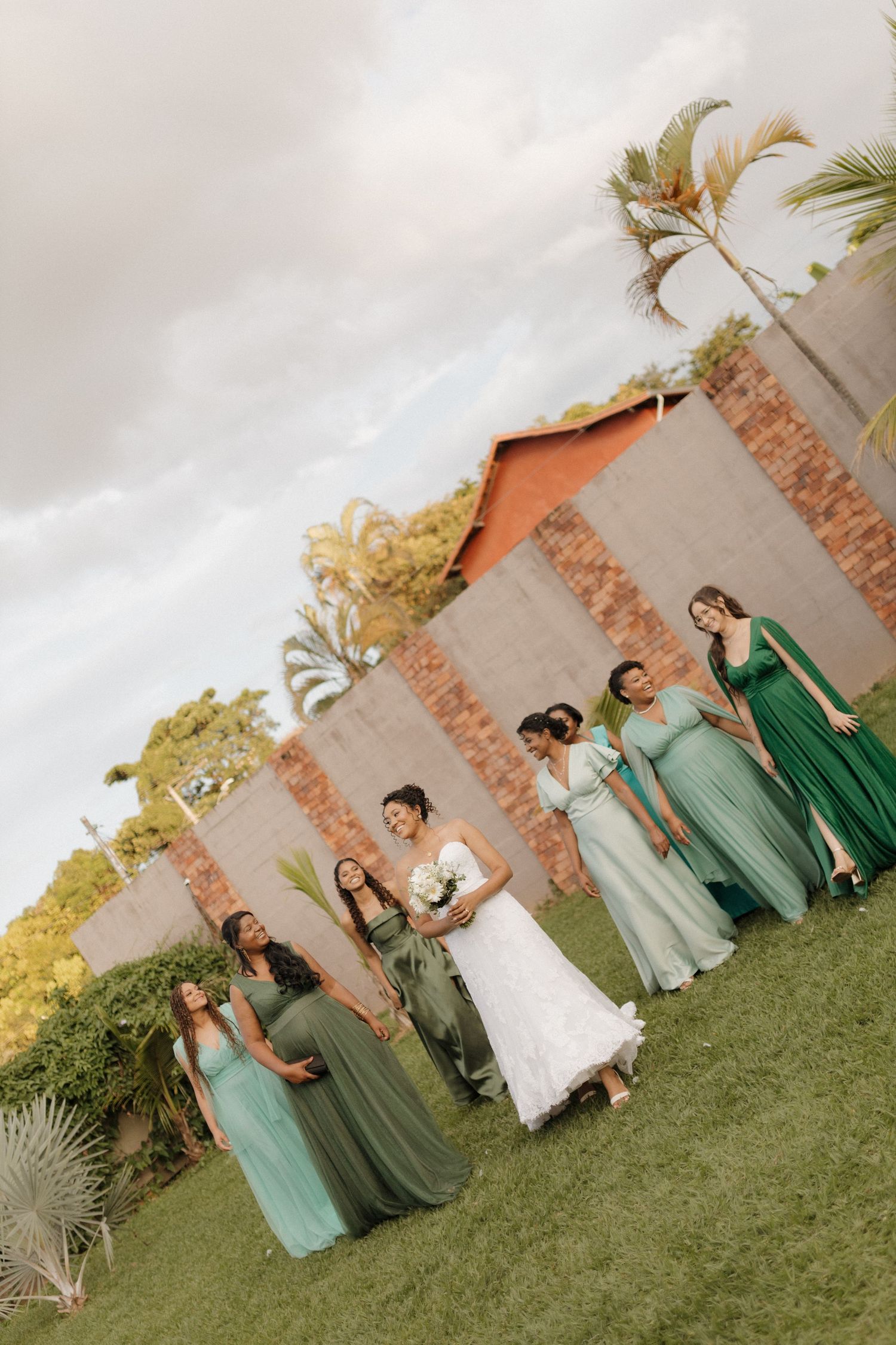 Wedding party in mint green dresses poses along brick wall in outdoor garden setting.