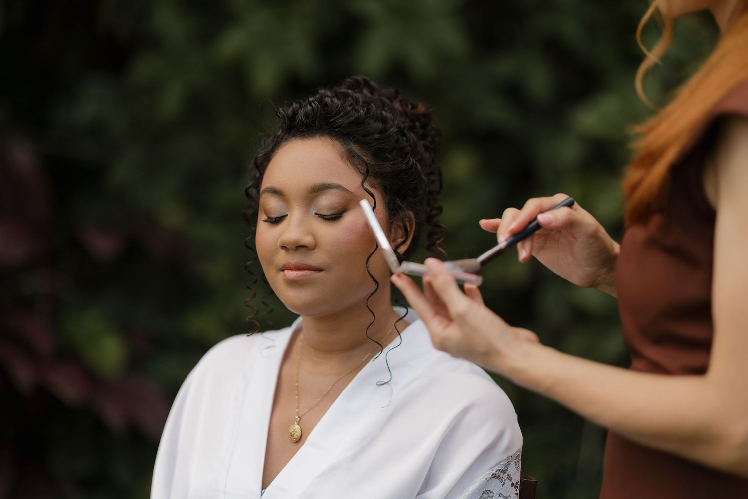 Professional makeup application in progress during wedding day preparations outdoors.