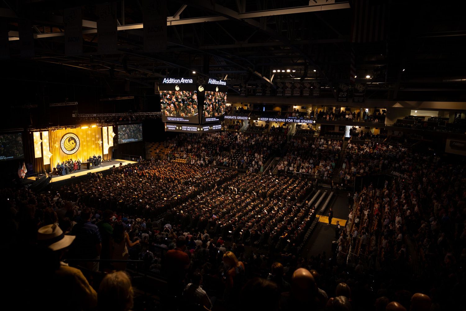 Large indoor arena filled with graduates during a university commencement ceremony.