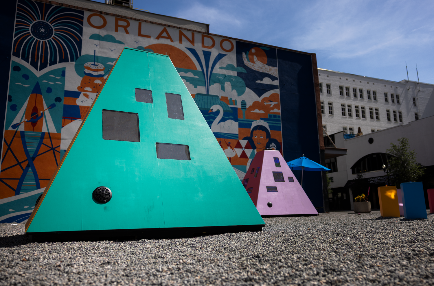 Colorful pyramid sculptures in front of an Orlando mural on the side of a building in downtown.