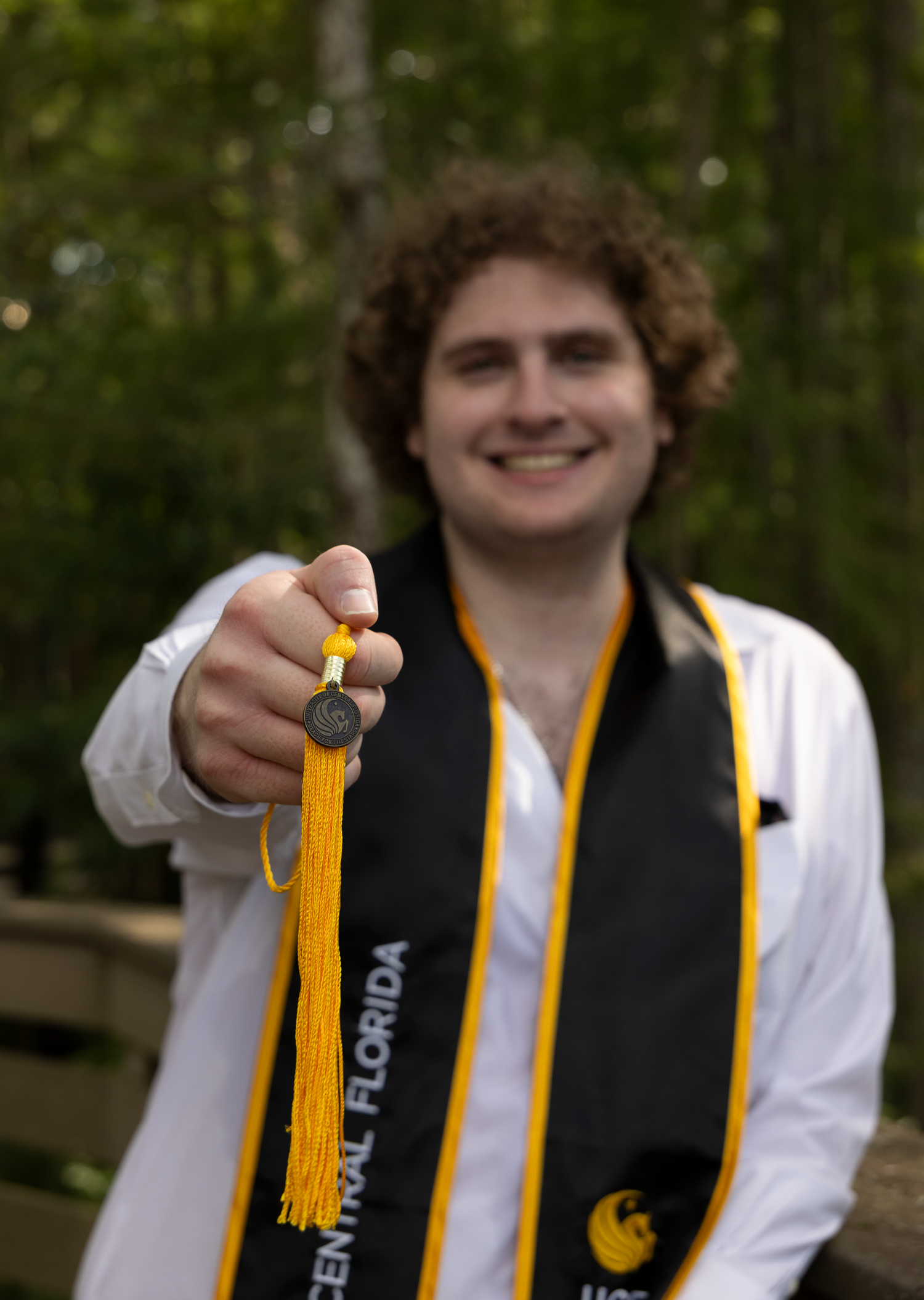 UCF graduate smiling outdoors holding a medal with black and gold University of Central Florida stole.