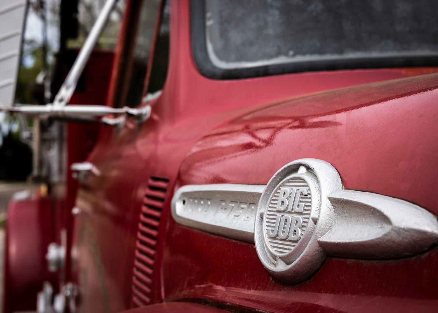 Close-up of a vintage red Big Job truck badge and hood ornament on a classic American pickup truck.