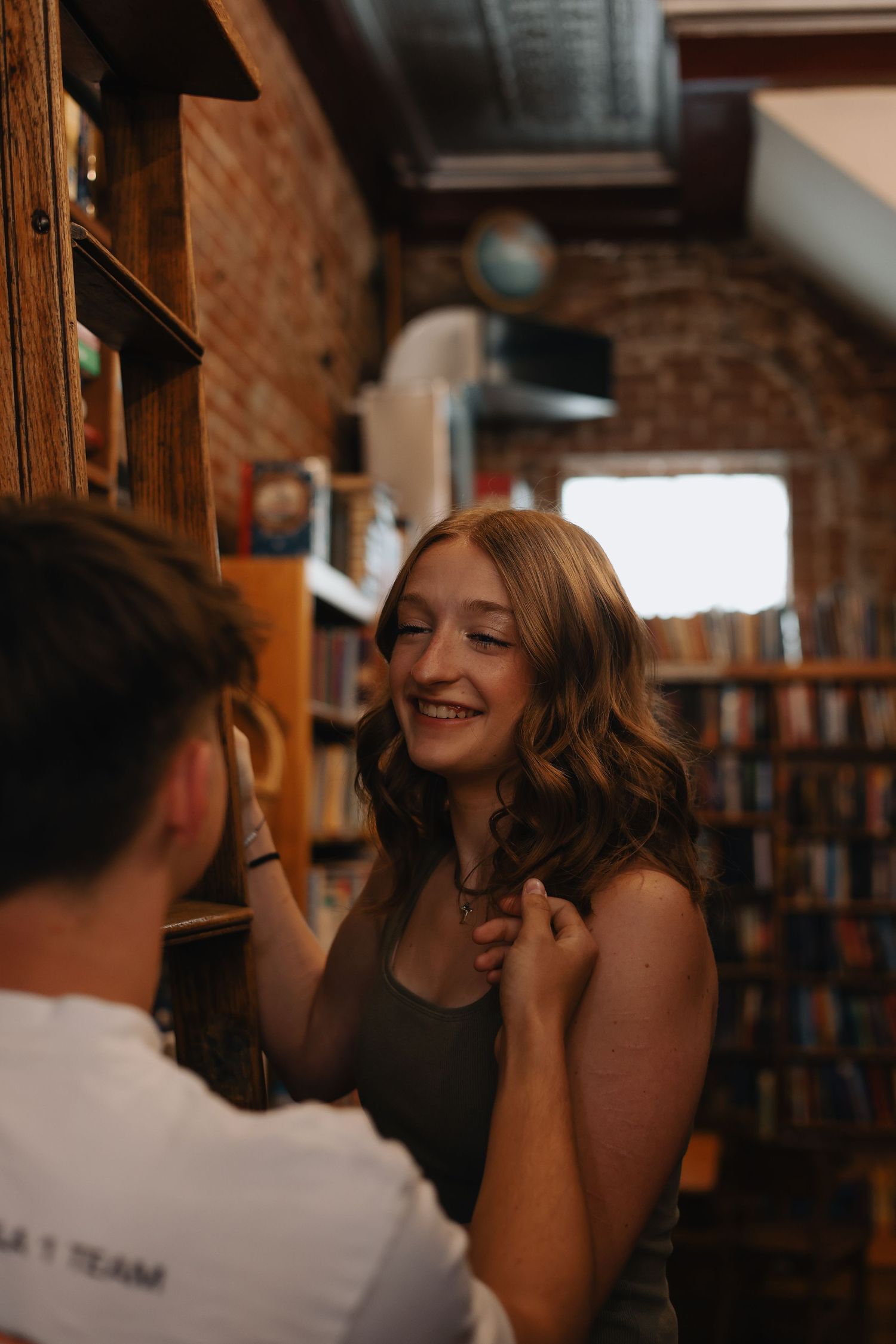 Couple sharing playful moment between library bookshelves.