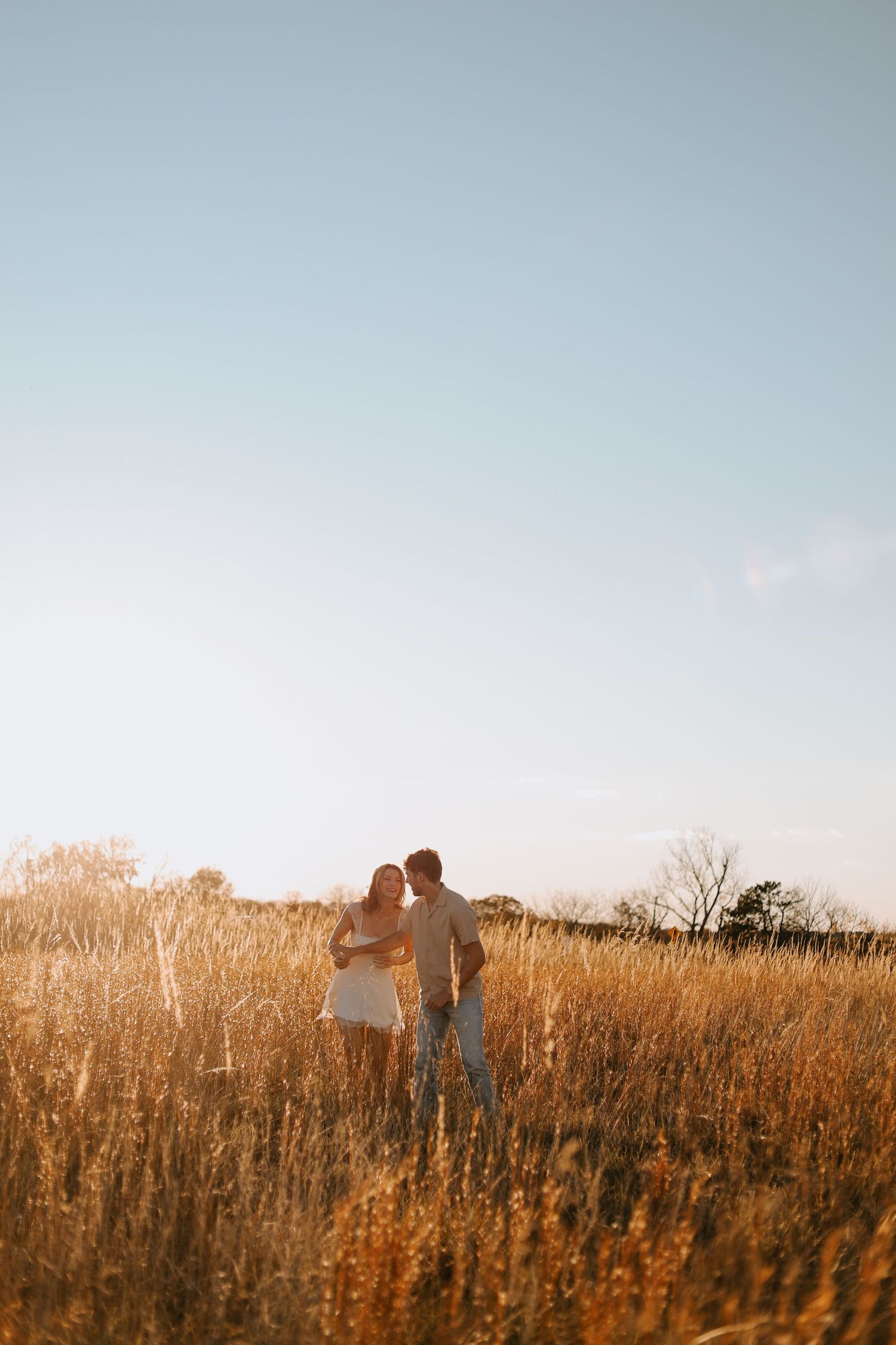 Two silhouettes stand together in a golden field at sunset.