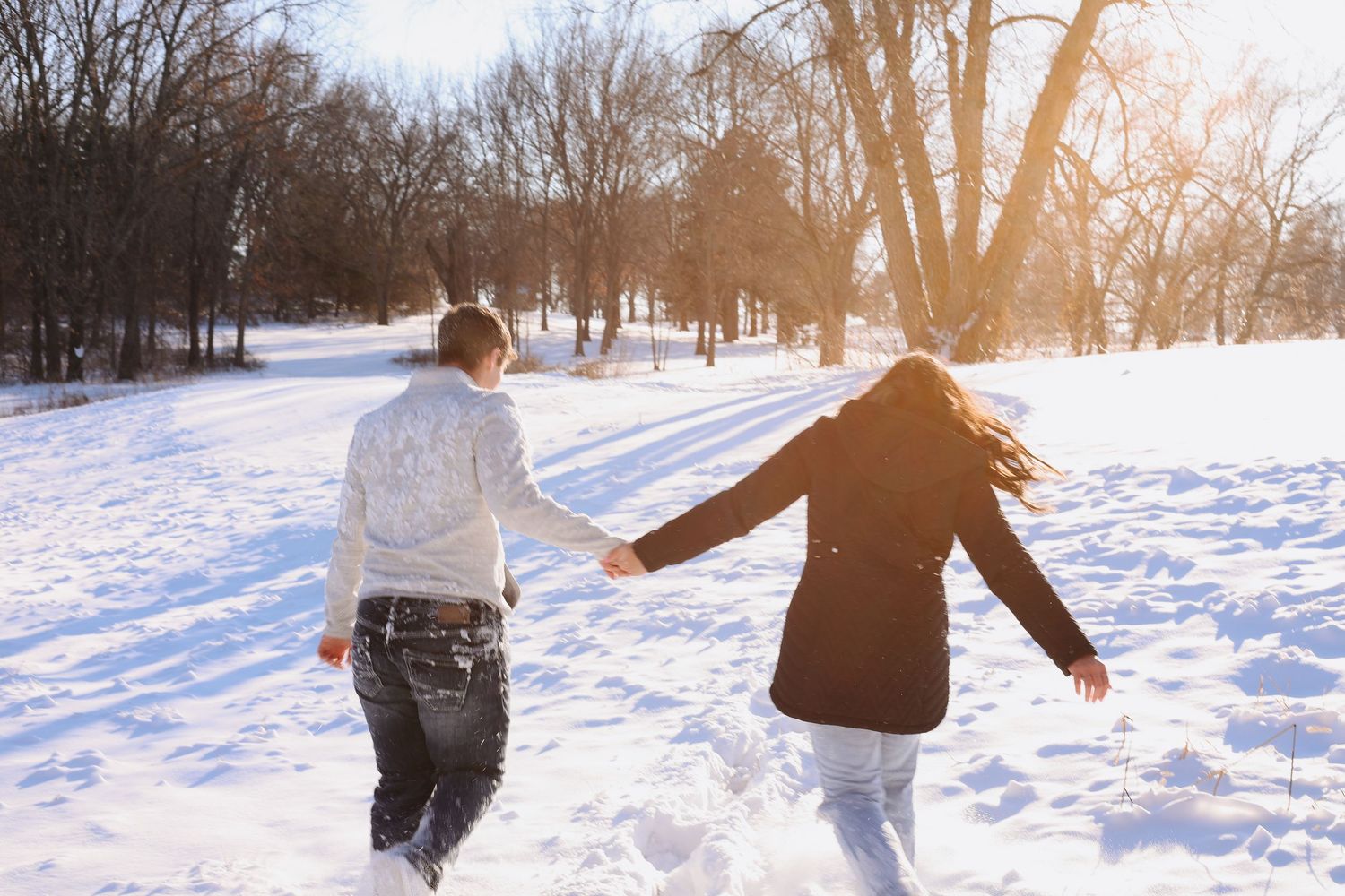 Two people walking hand in hand through a snowy winter landscape at sunset.