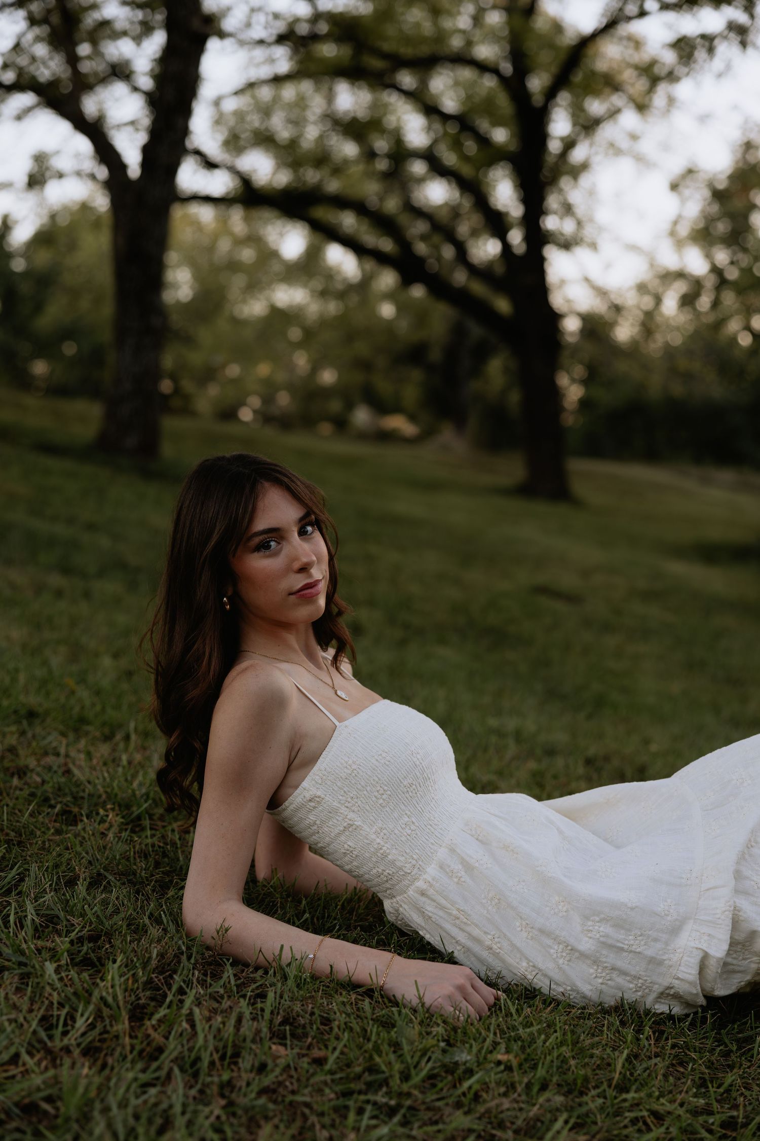 A dreamy outdoor portrait of someone in a white dress lying on grass during golden hour.