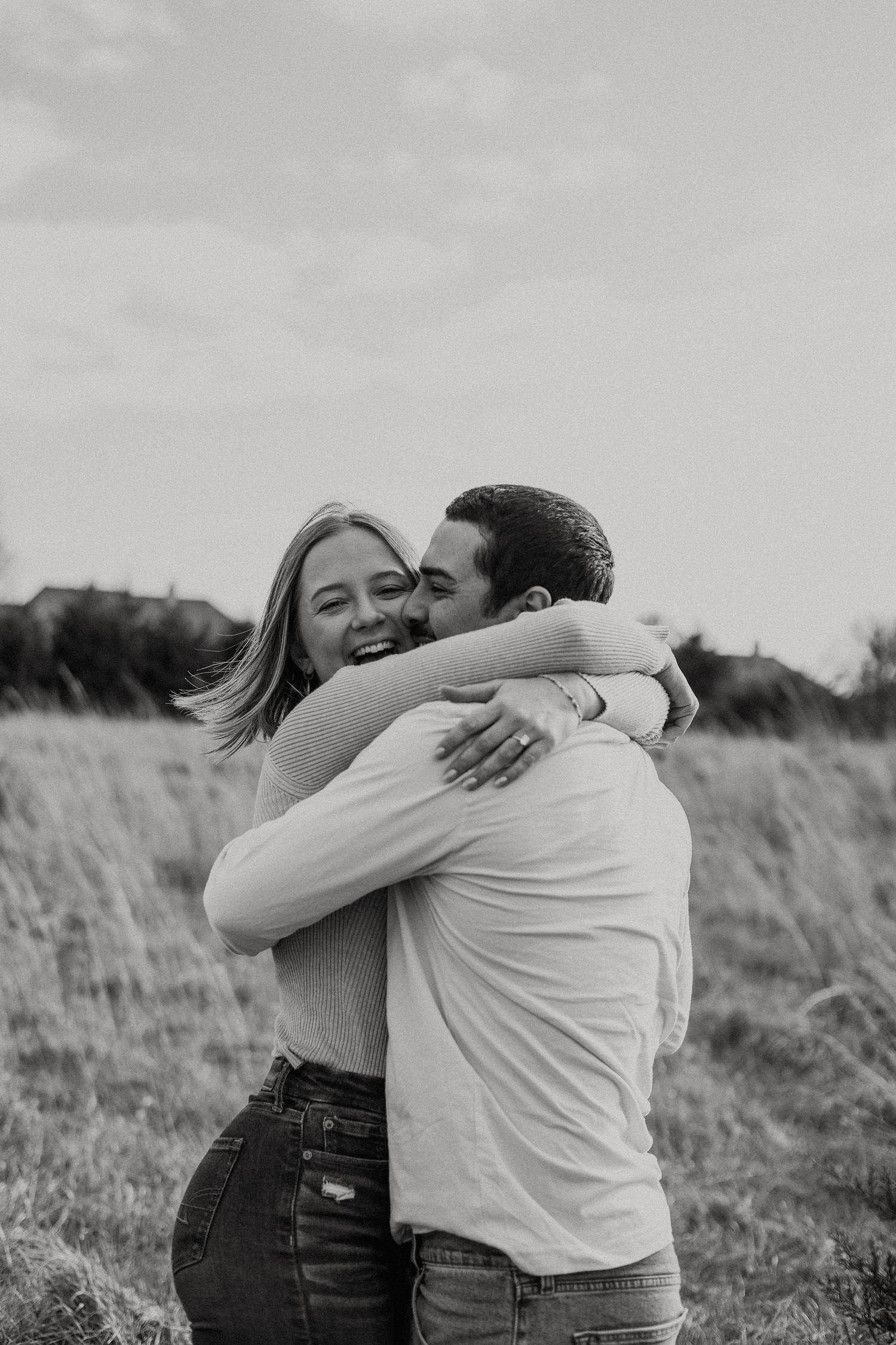 Couple embracing in a field with tall grass on an overcast day.