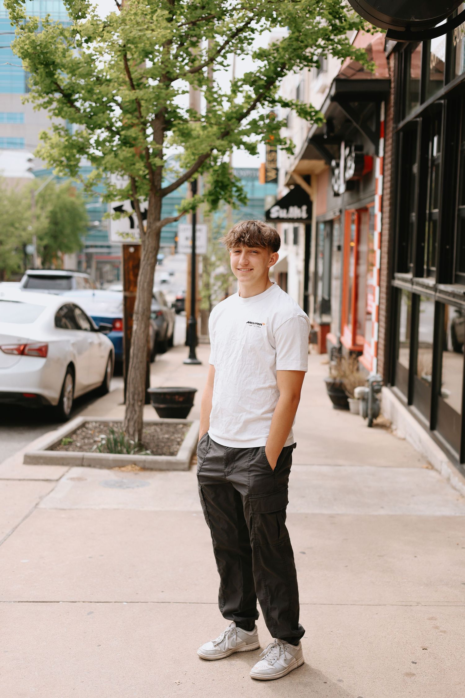 A casual urban scene showing someone sitting on a sidewalk bench wearing white sneakers and dark pants.