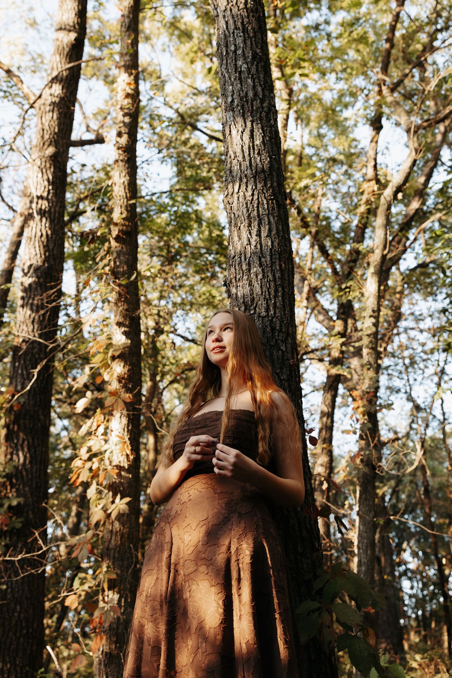 A golden hour portrait among tall trees holding a coffee cup.