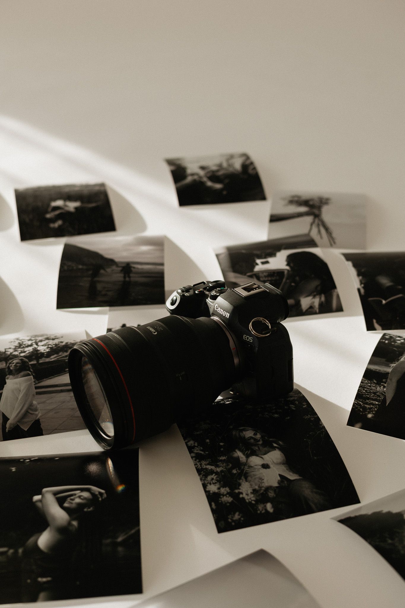 Professional camera surrounded by black and white photographs spread on white surface.