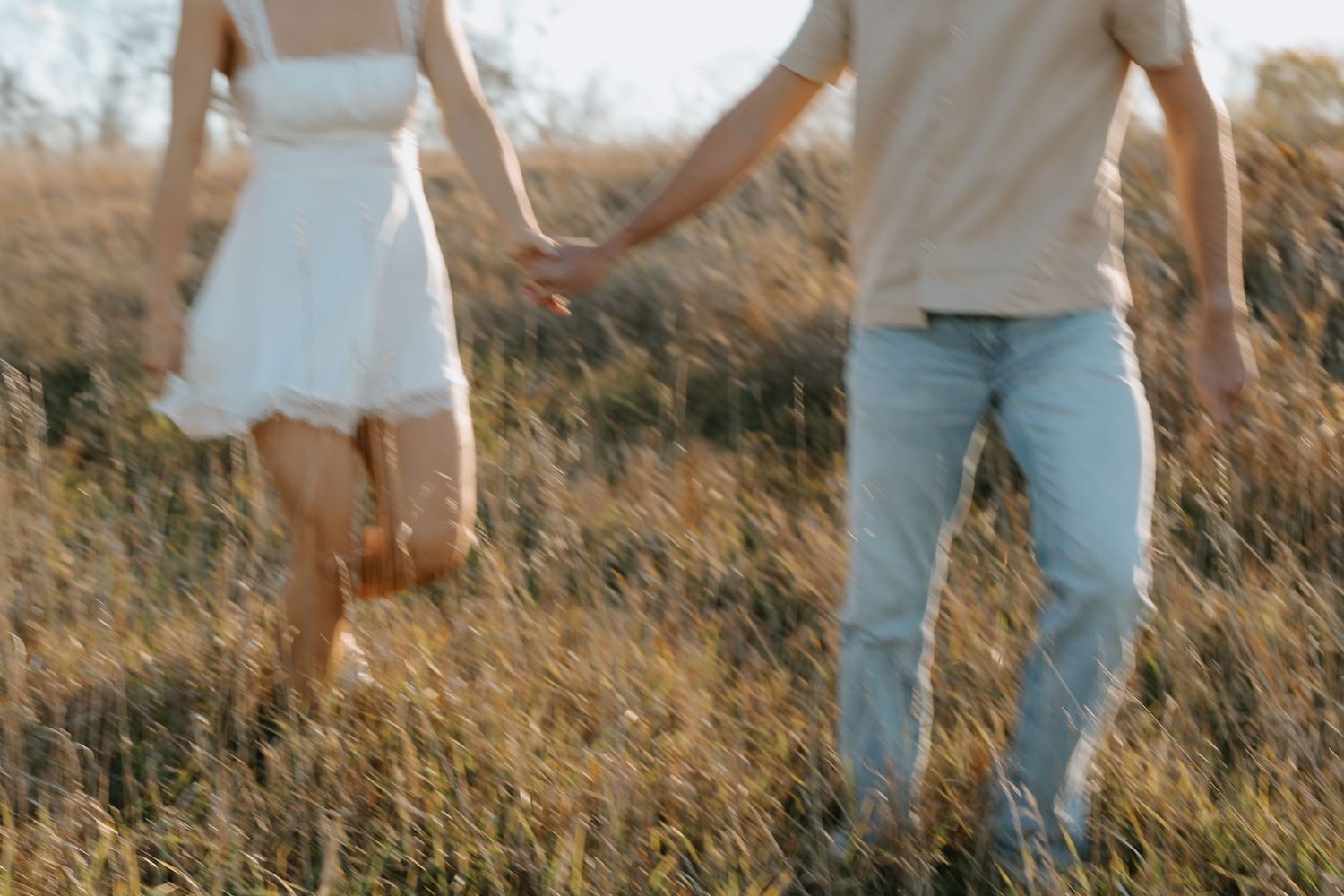 Cropped view of two people walking through tall grass at golden hour.