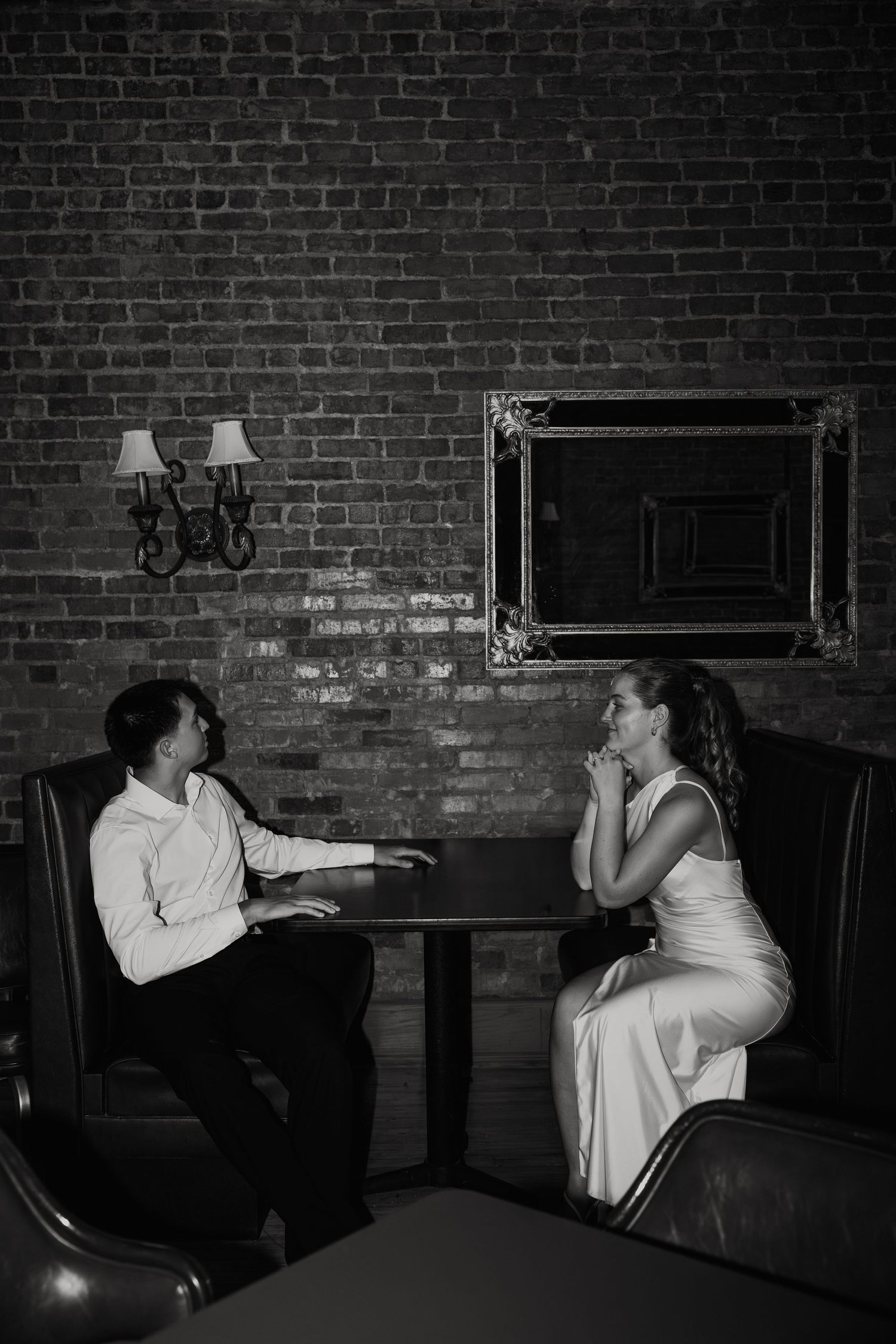 A couple having an intimate conversation at a table in a dimly lit restaurant with exposed brick walls.