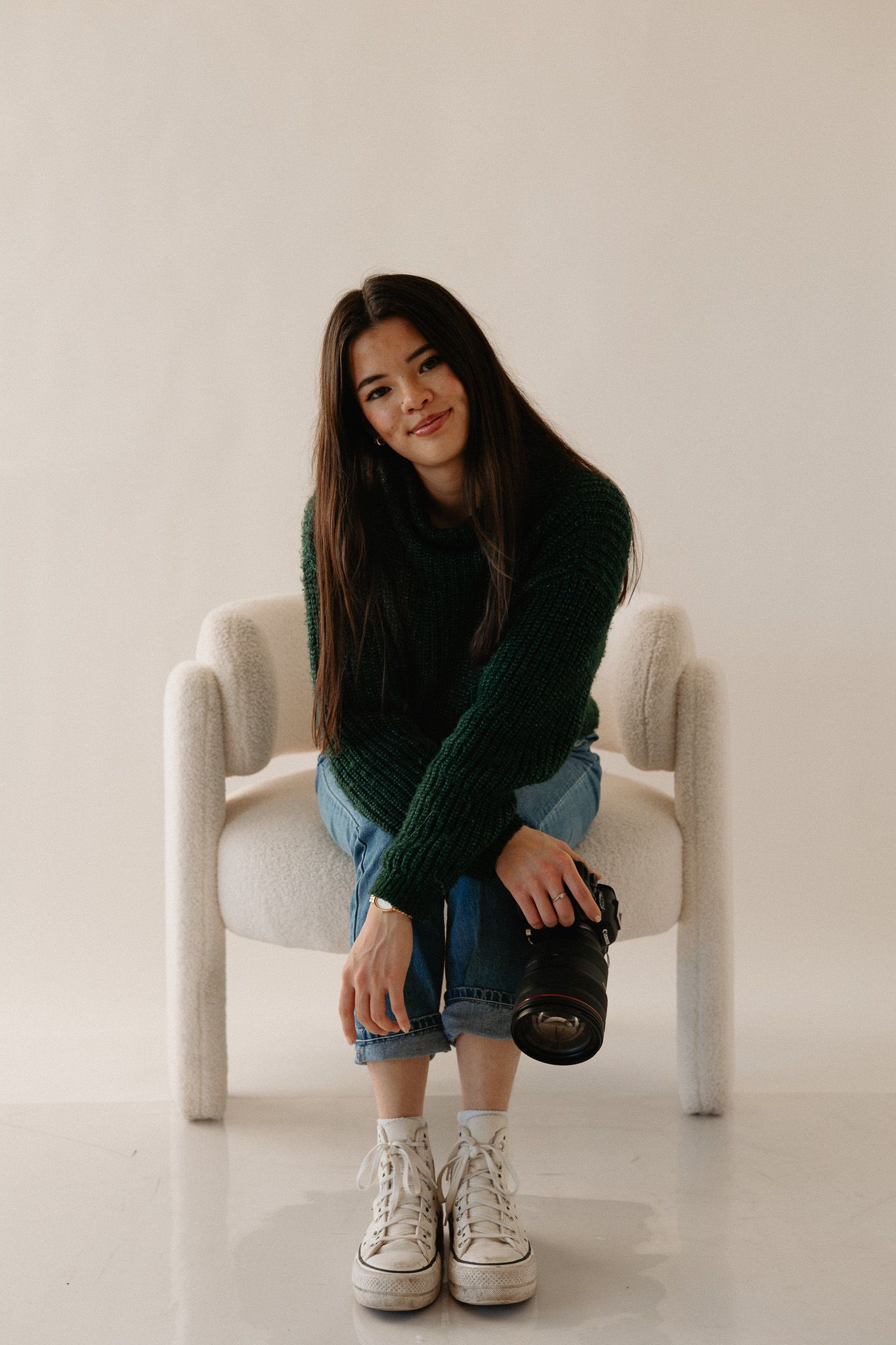 Person in dark sweater and jeans sitting on white chair in minimalist setting.