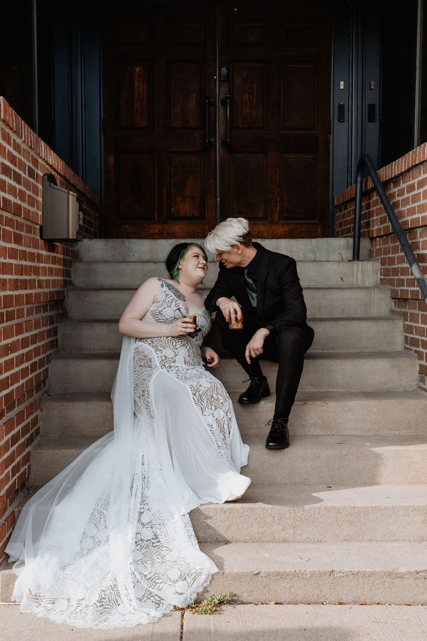 Wedding couple sitting on concrete steps against a brick wall.